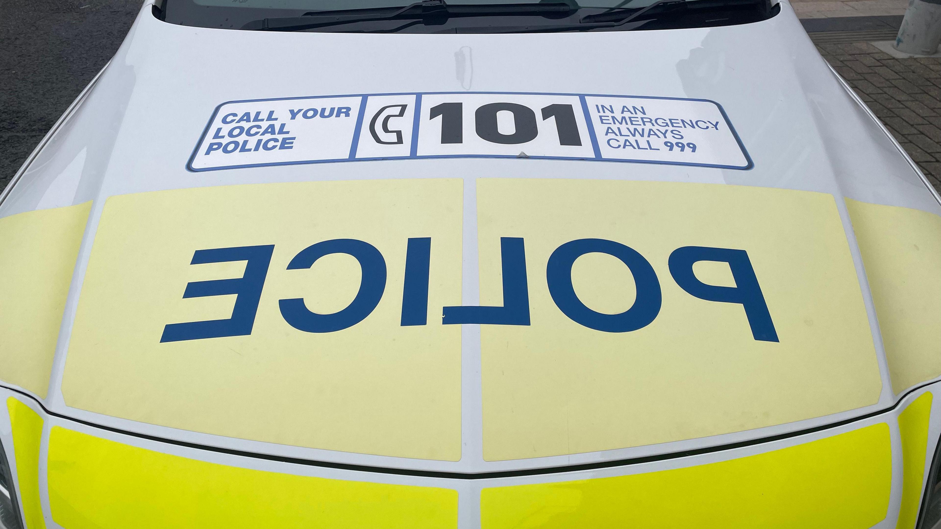 Yellow and white police car bonnet with police written in blue block capitals and a banner saying call 101.