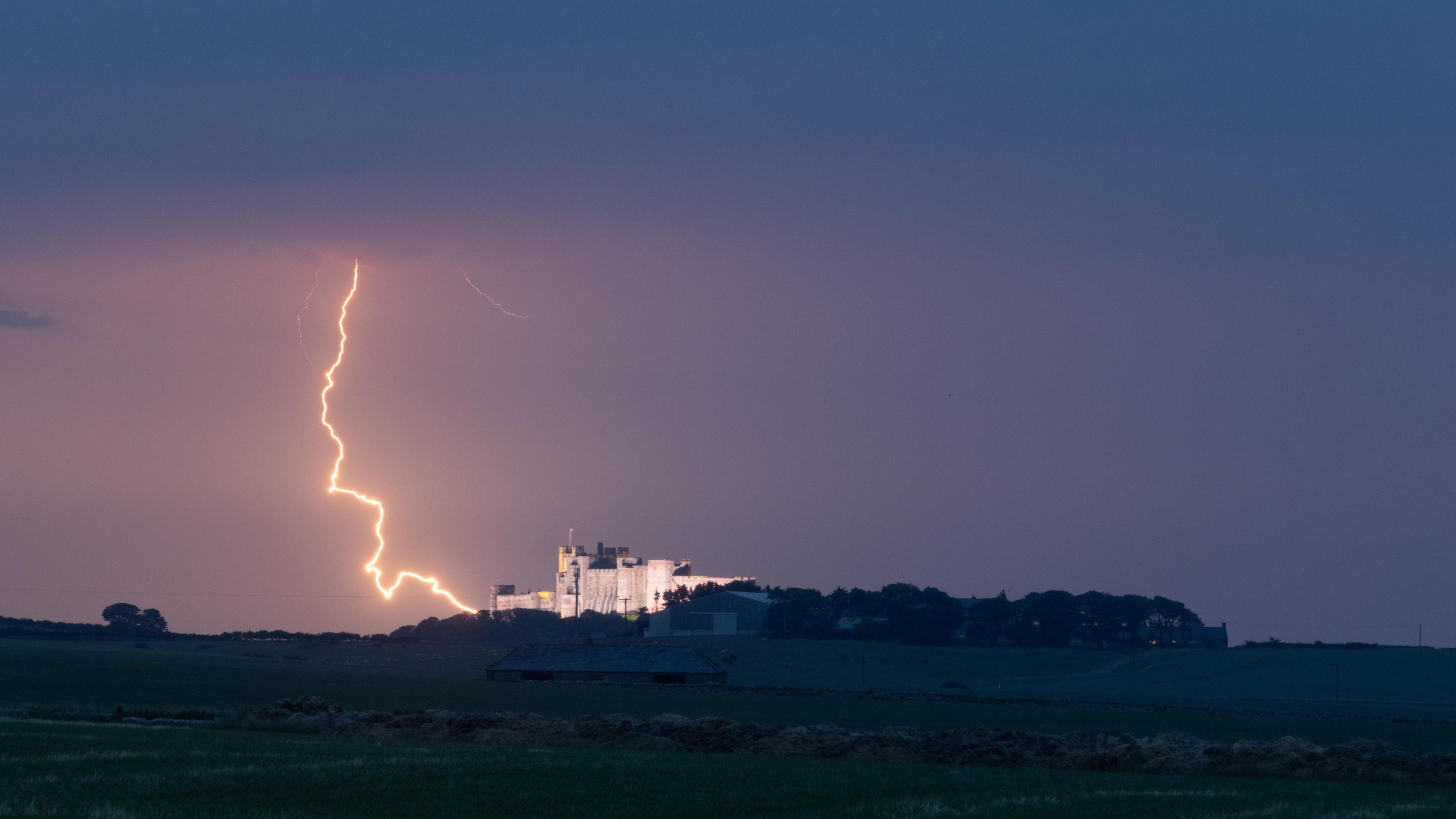 A landscape image of a bolt of lightening striking down behind a building that looks like a castle.