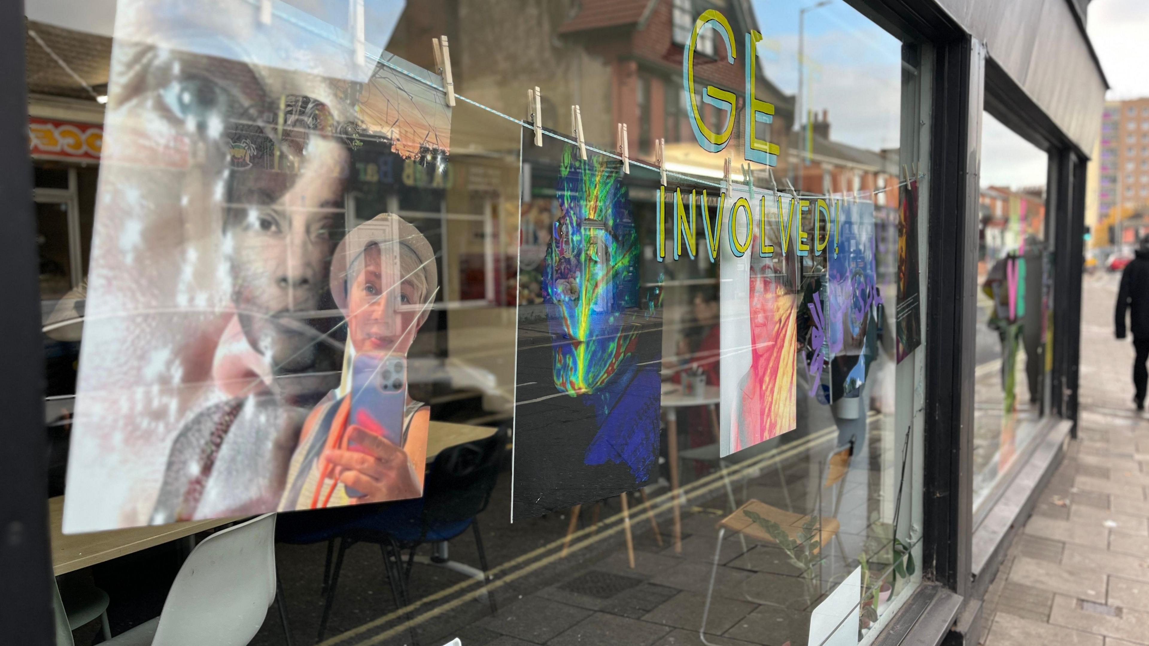 Photos of women hung in a window, viewed through the glass from the street