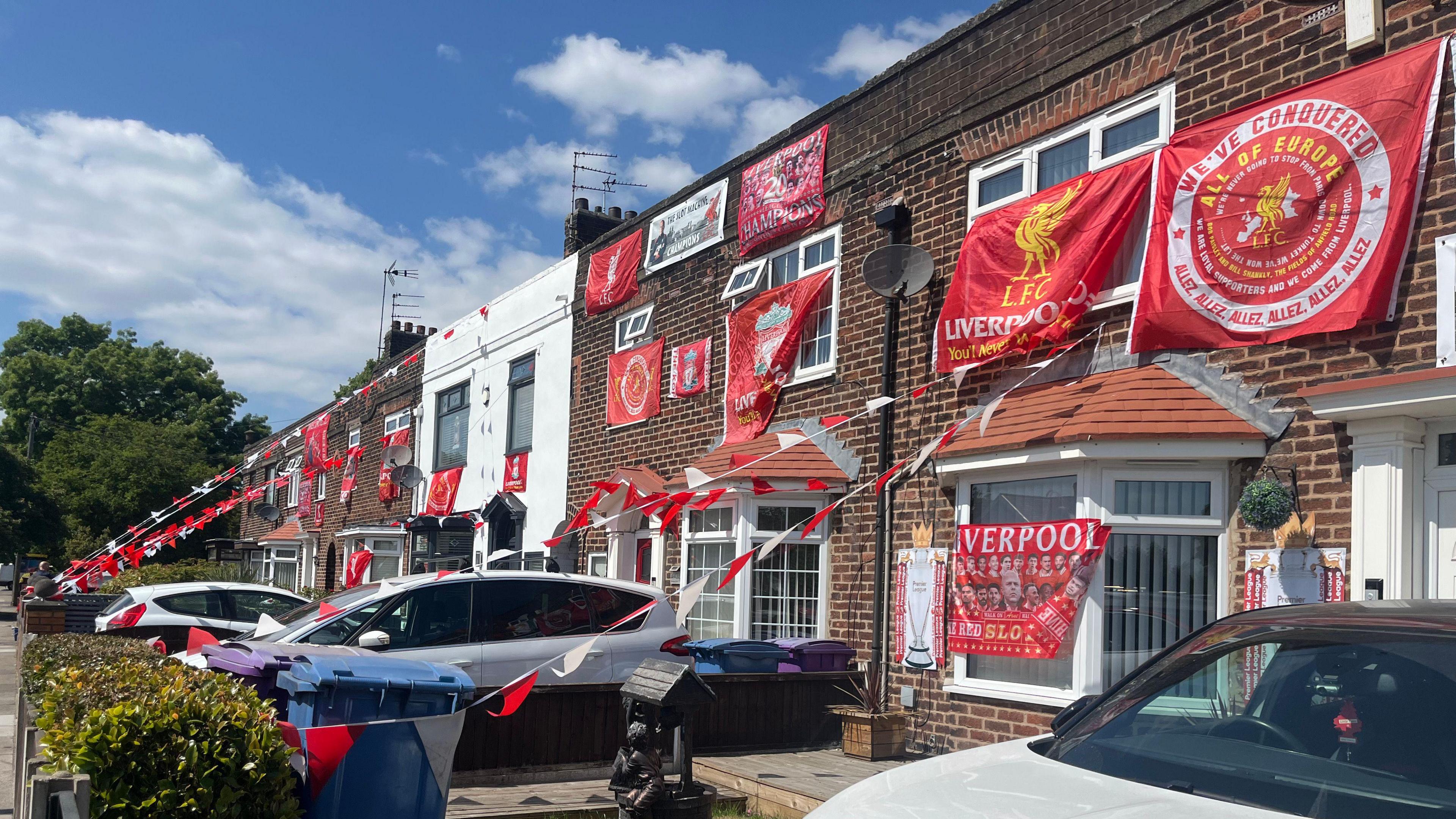 A row of terraced houses draped in red and white Liverpool flags, bunting and banners