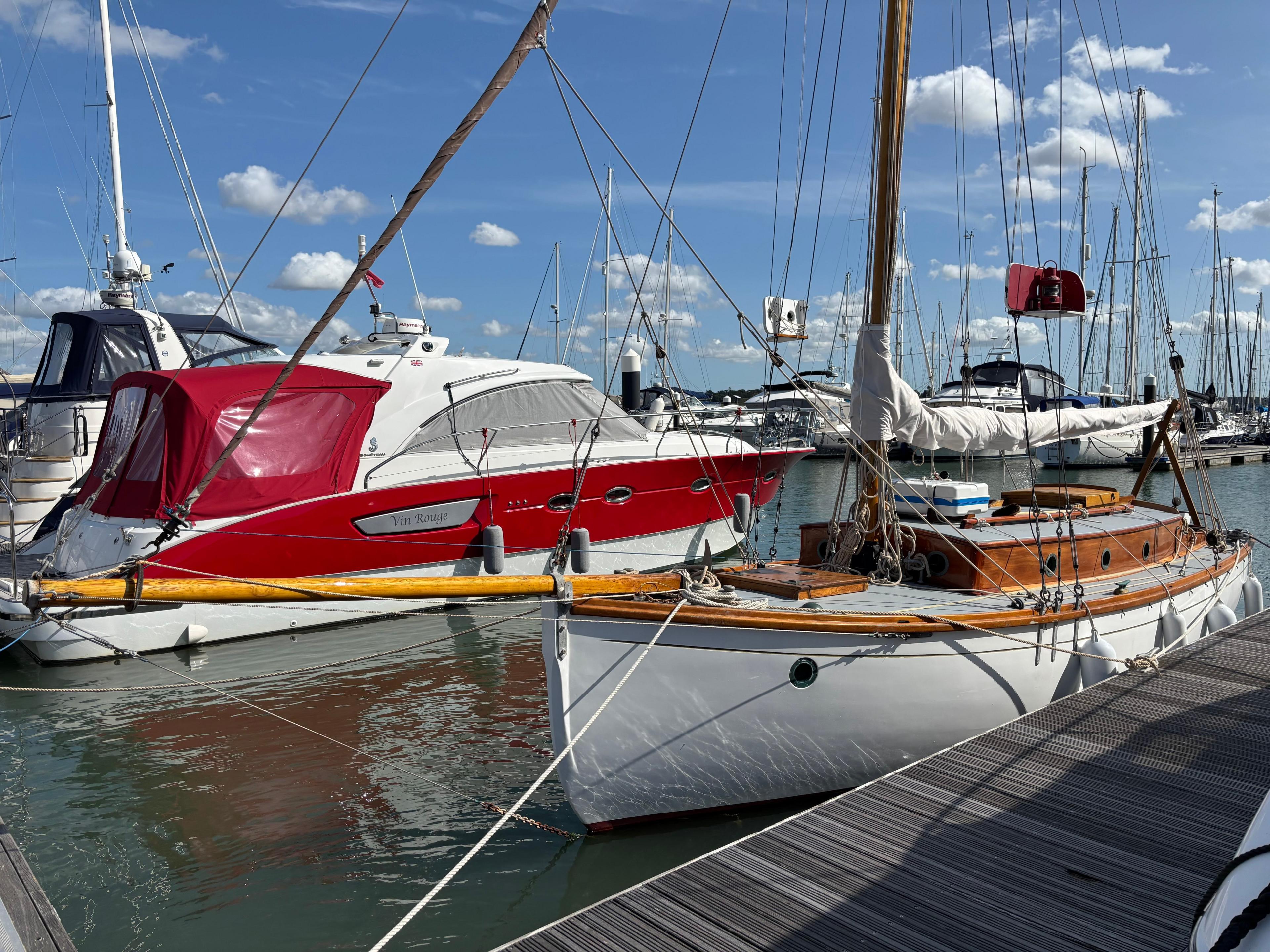 Another side view of Nancy Blackett moored to the wooden boardwalk. Other yachts can be seen in the background, floating on the water.