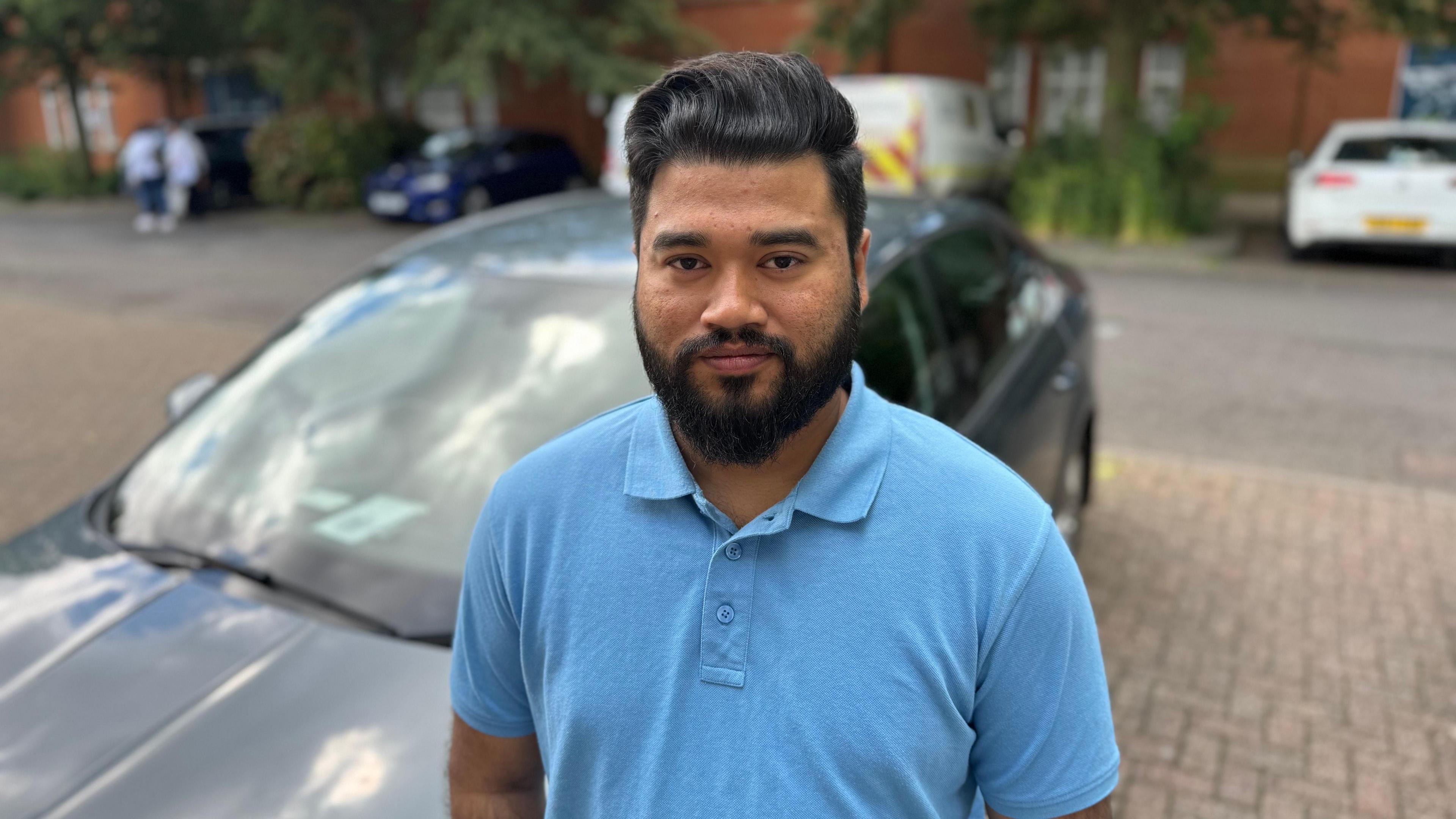 Yusuf Rabbi in Ipswich standing in front of a parked car