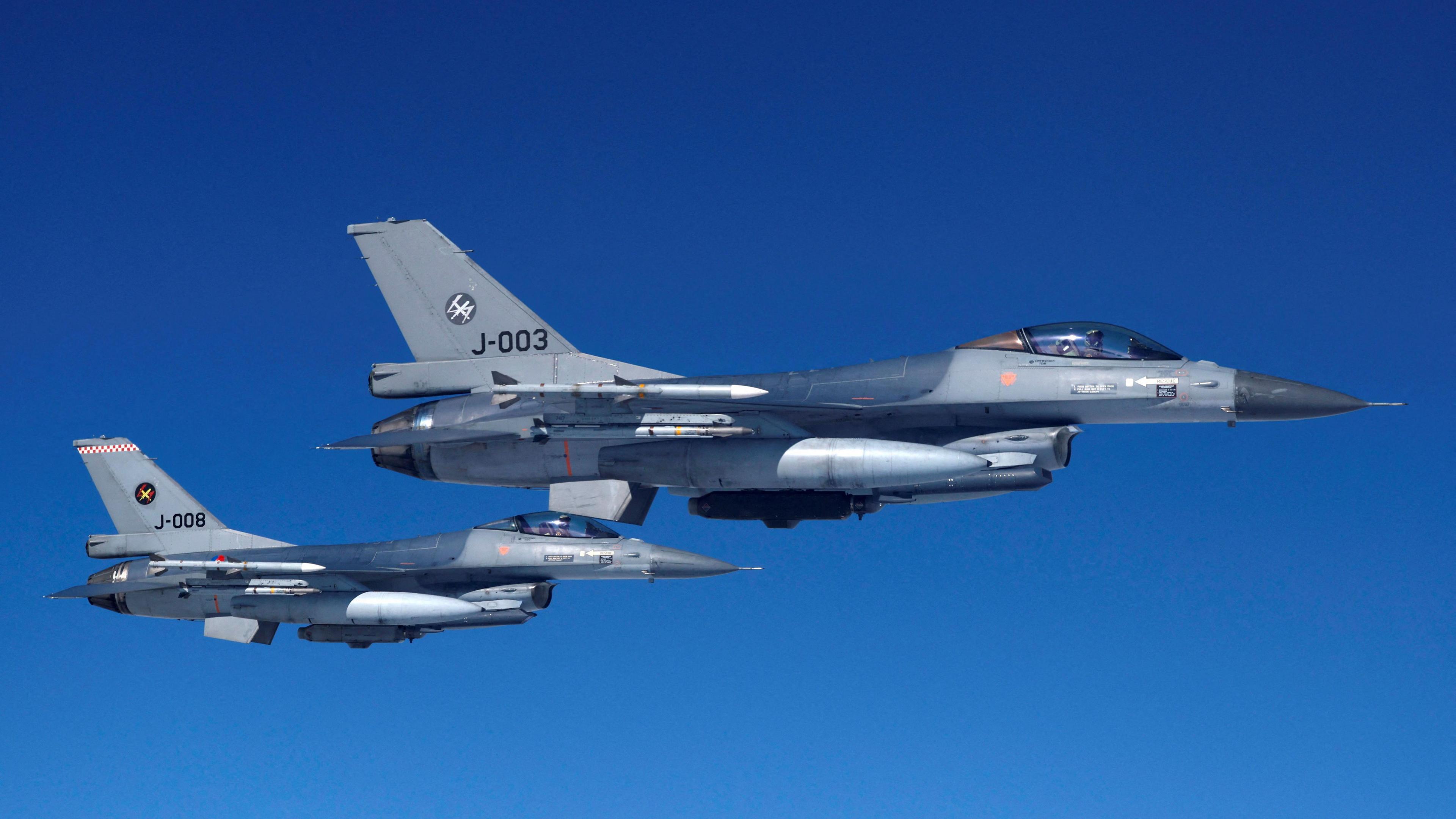 Two F-16 jets painted gray and blue flying in the blue sky