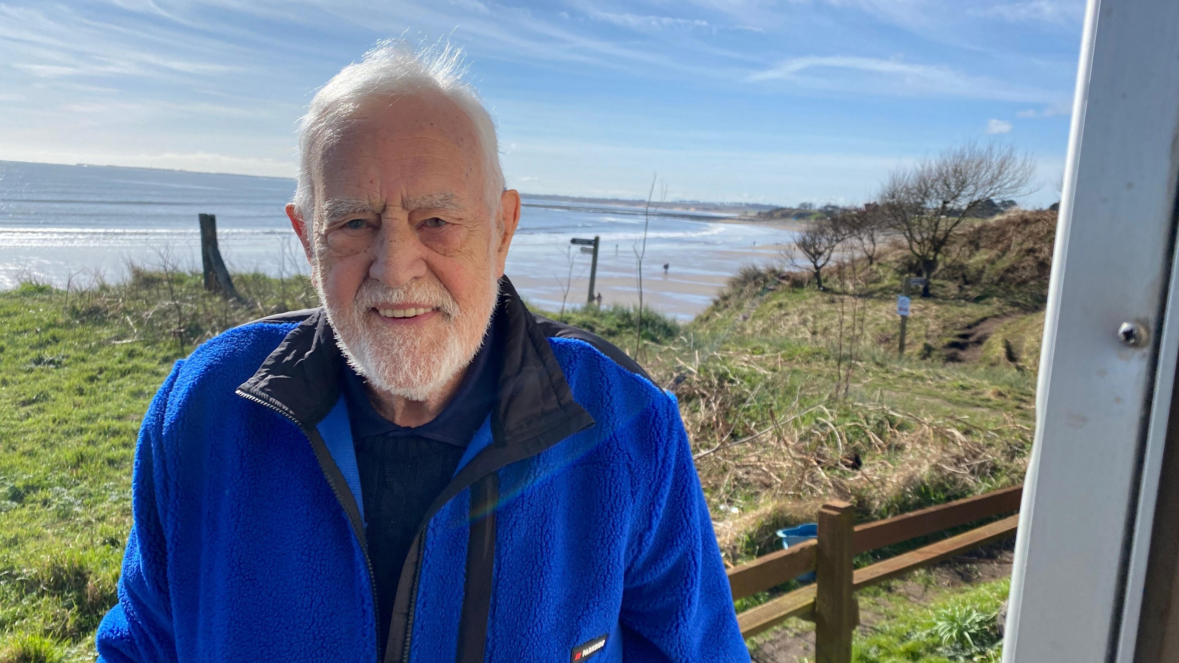 A man standing in front of a beach from the door of his caravan