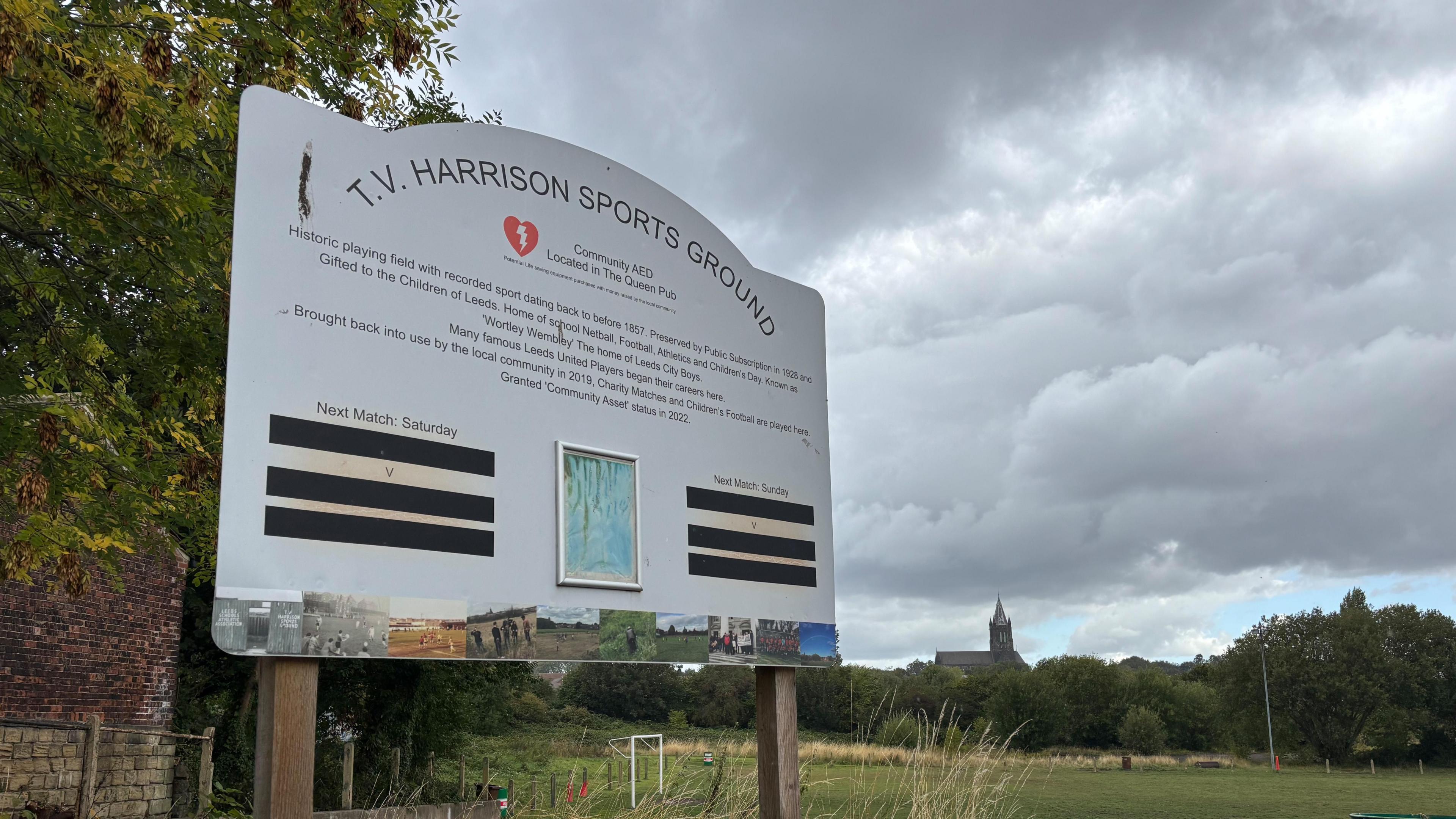 A sign which reads T.V. Harrison Sports Ground with a football field in the background.