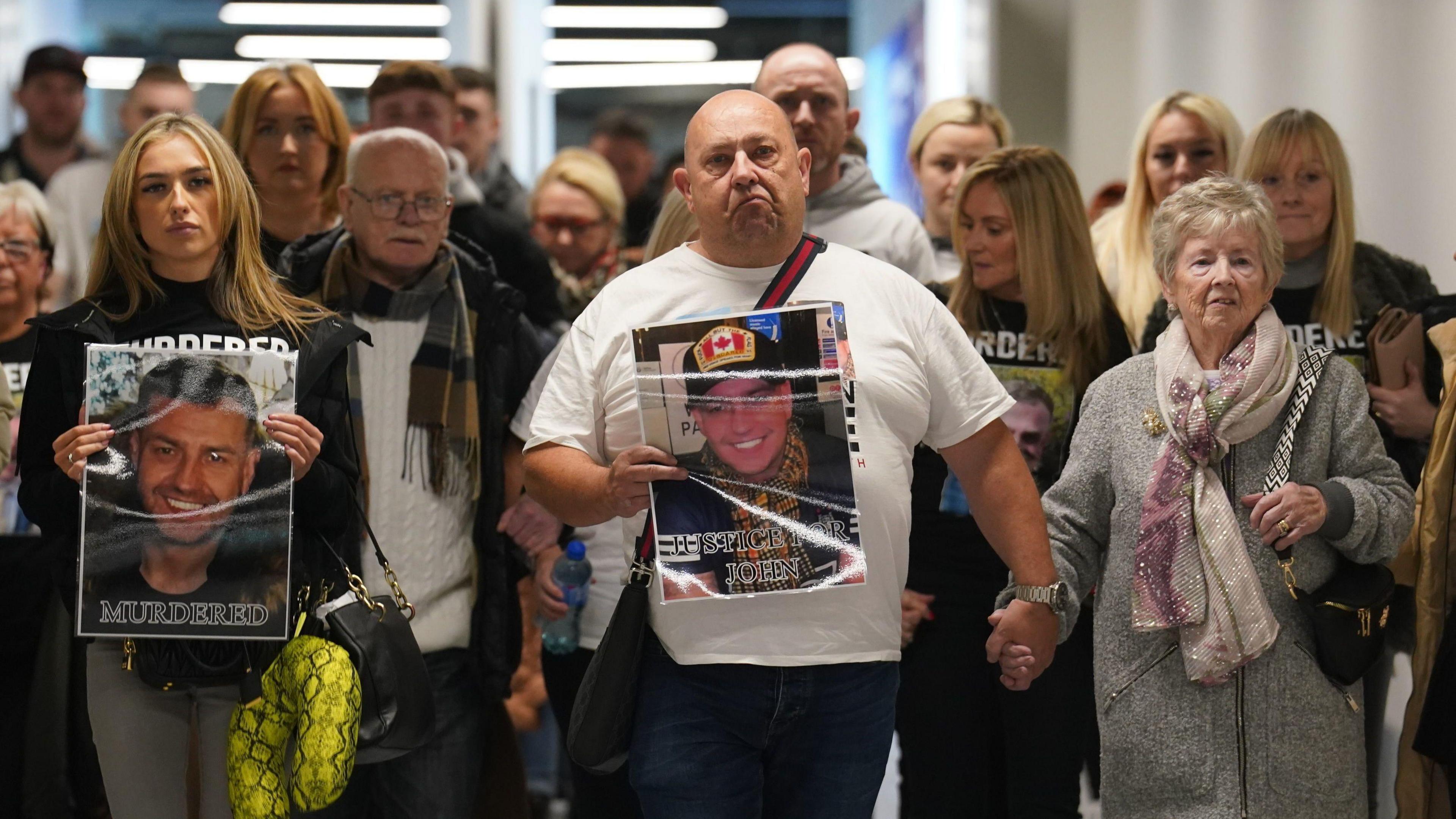 A large crowd of people walking down a corridor holding posters with pictures of John George