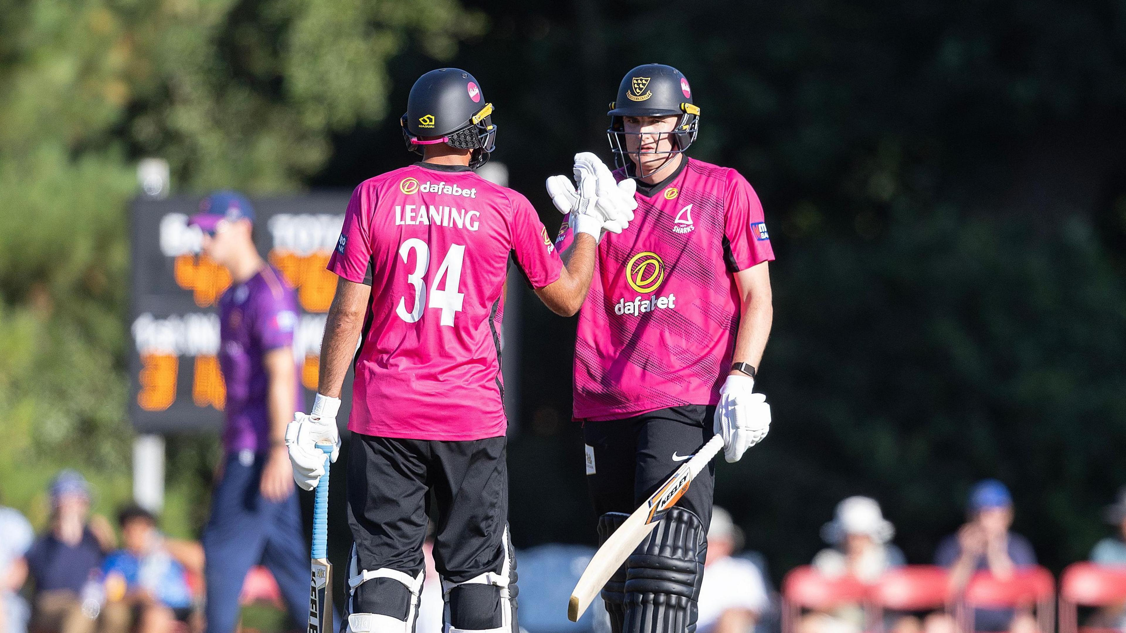 Jack Leaning, wearing the pink shirt of Sussex, shakes hands with captain Jack Carson during the win over Essex