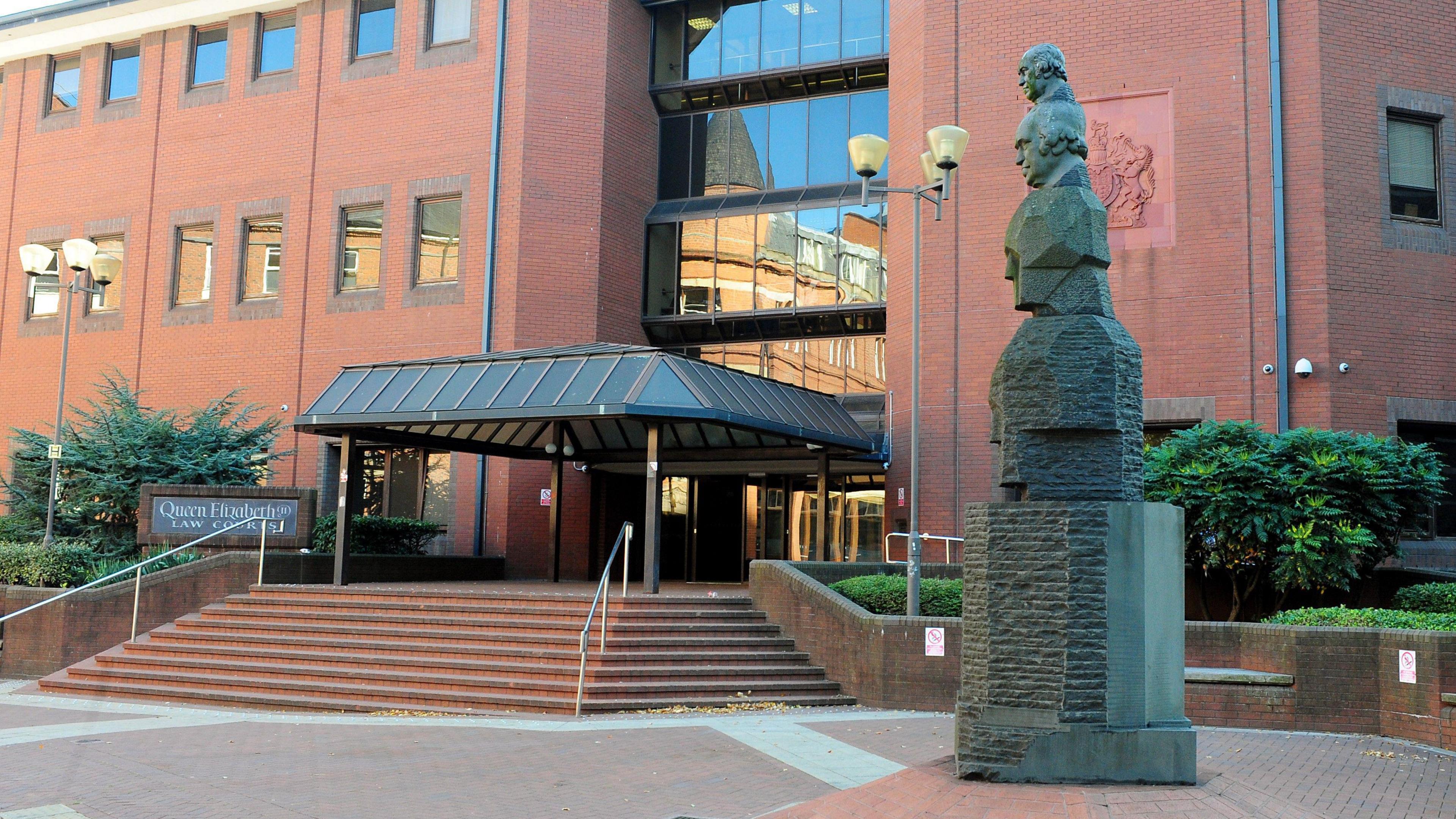 A general view of Birmingham Crown Crown exterior. The picture shows a large red building with steps leading up to a covered entrance. A statue sits below the steps and windows line the building.