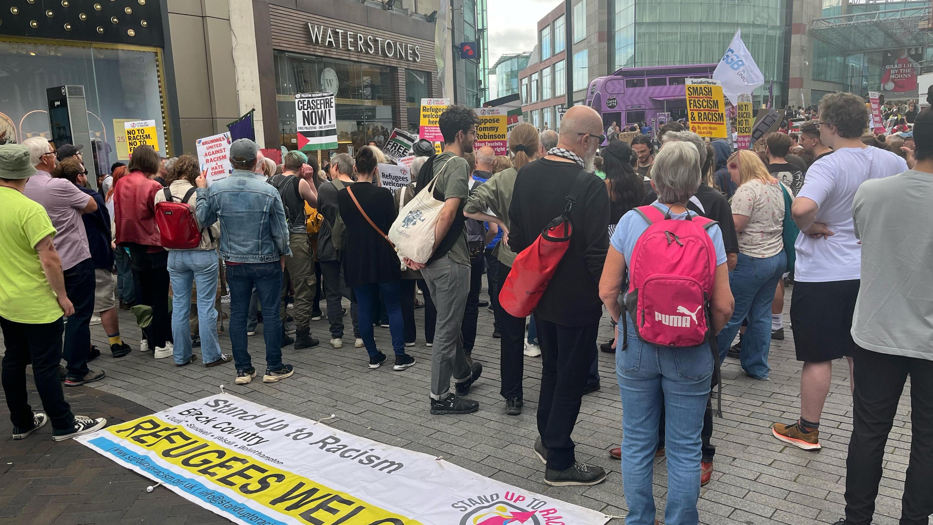 A stand up to racism banner lies on the ground behind crowds of protesters with signs