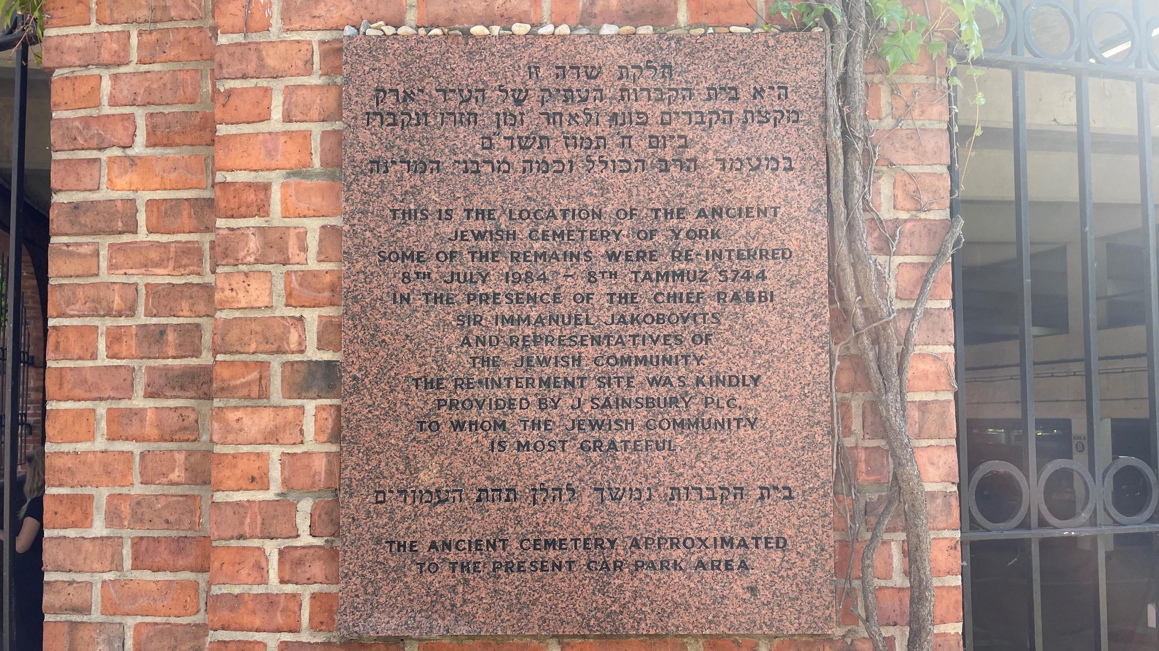 A stone plaque on the wall of a car park in both Hebrew and English.