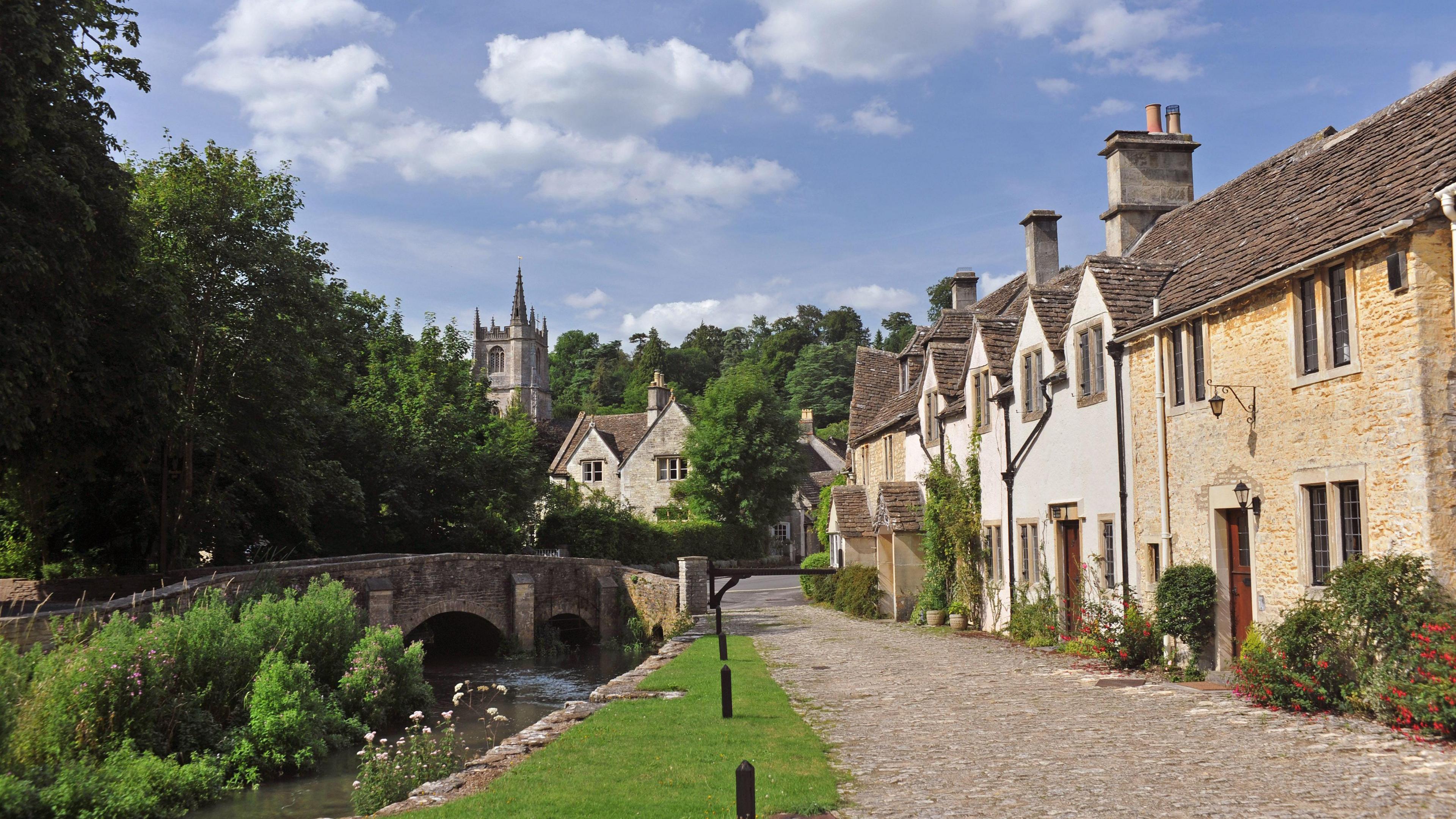 A picturesque village with a row of house, a cobble lane, a river and a stone bridge. In the background, there is a church.