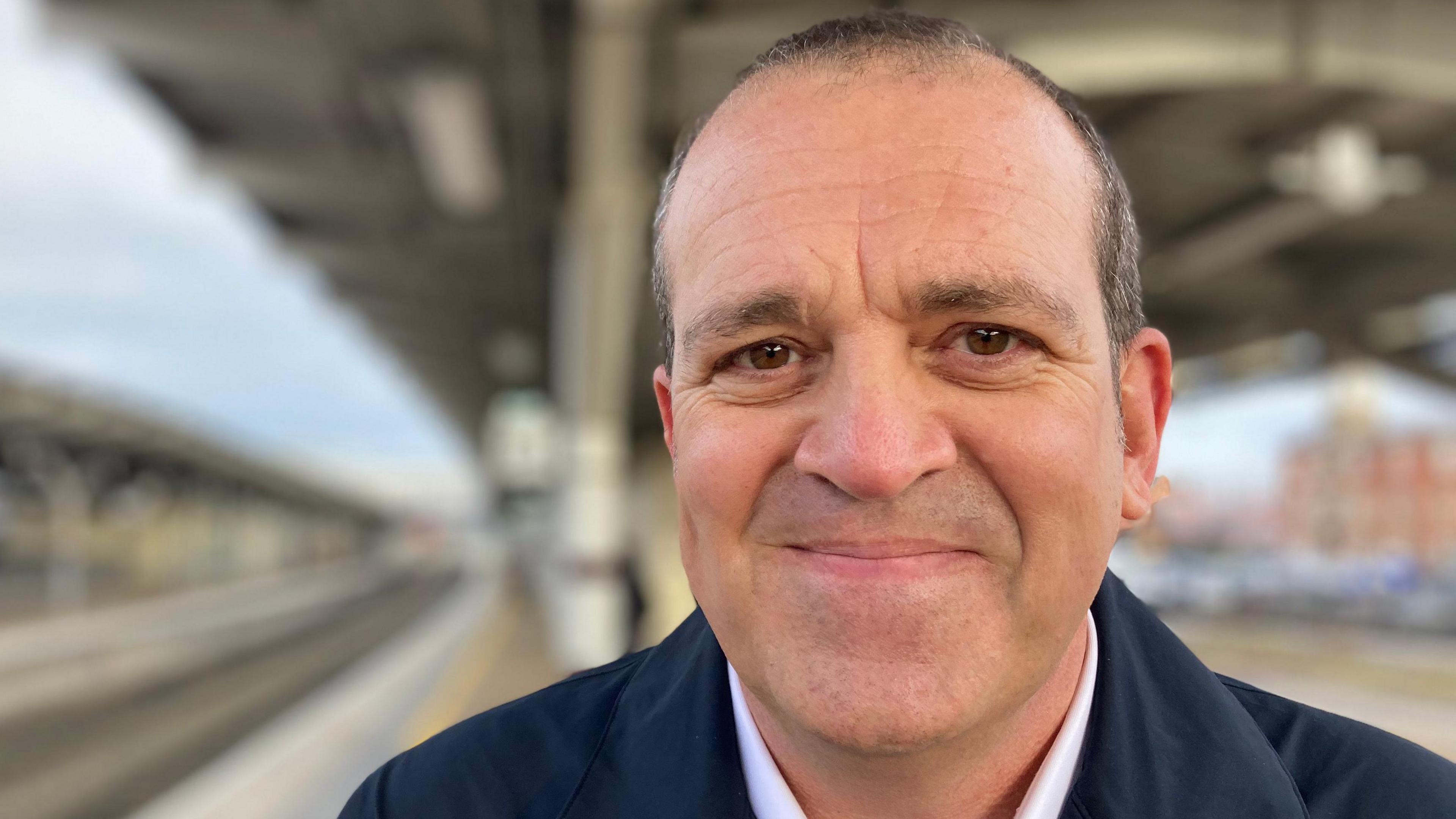 A man with short hair, brown eyes and wearing a navy blue jacket