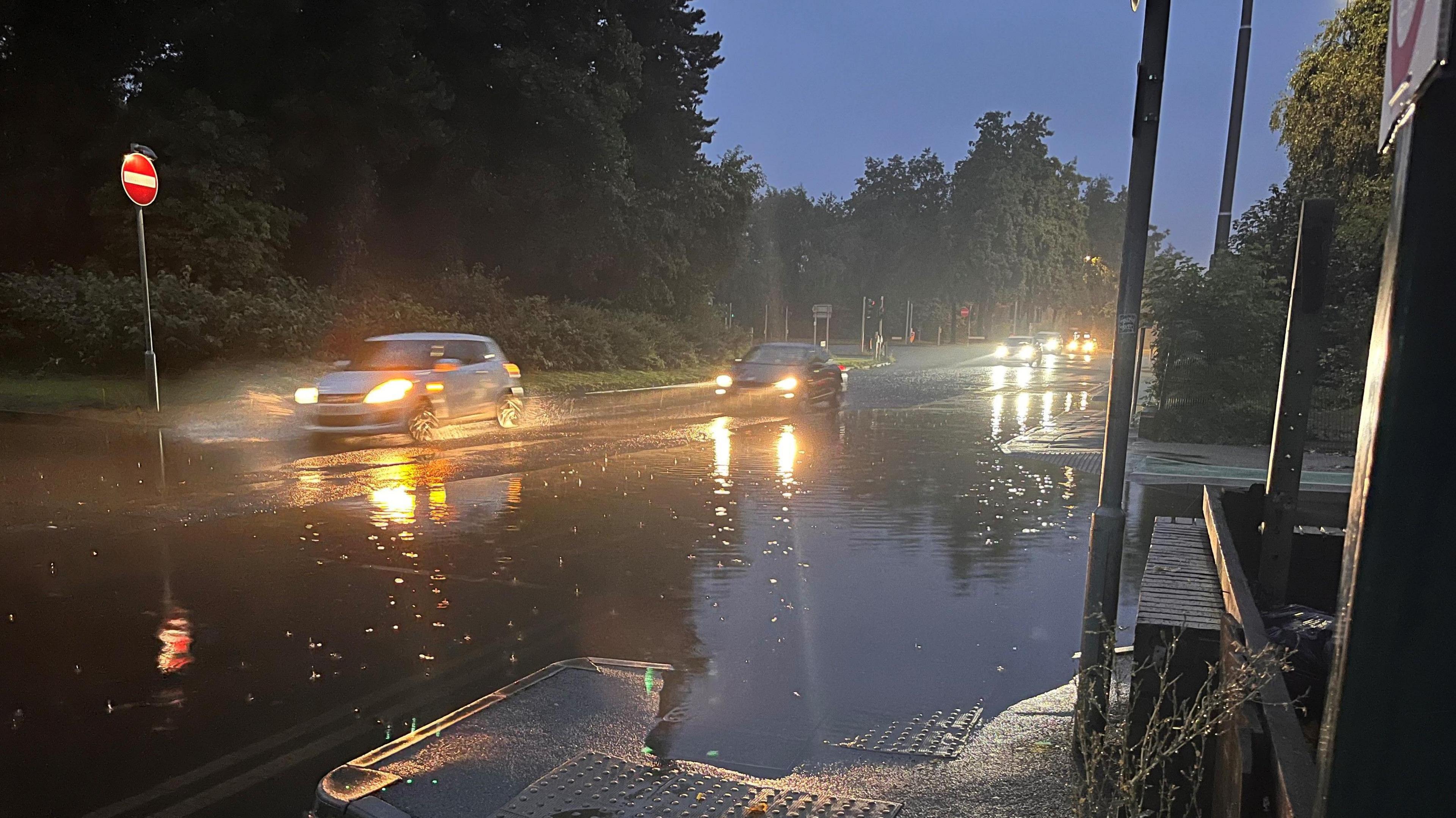 Cars with their headlights on driving through floodwater on a road