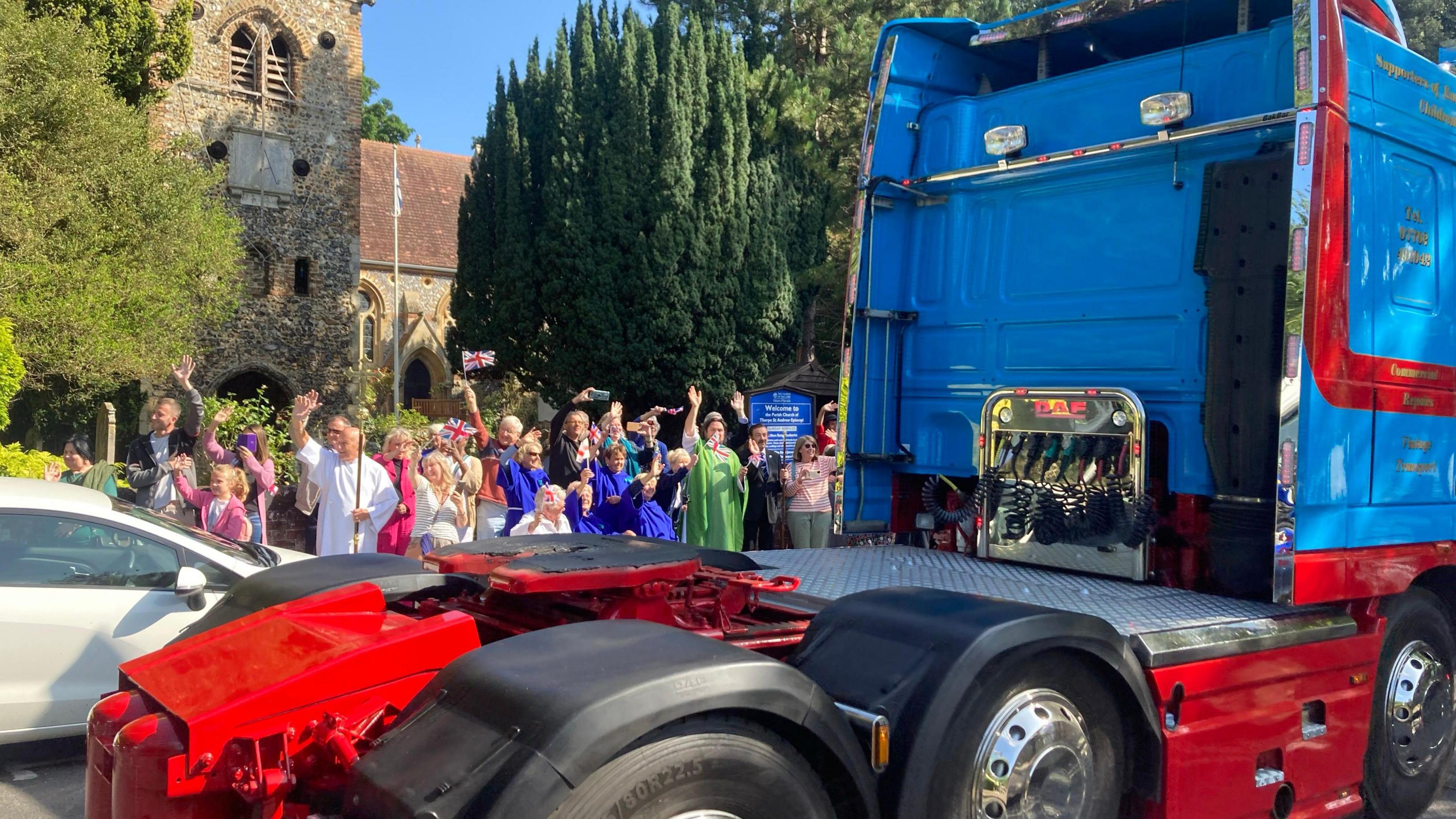 People wave as a truck passes by a church