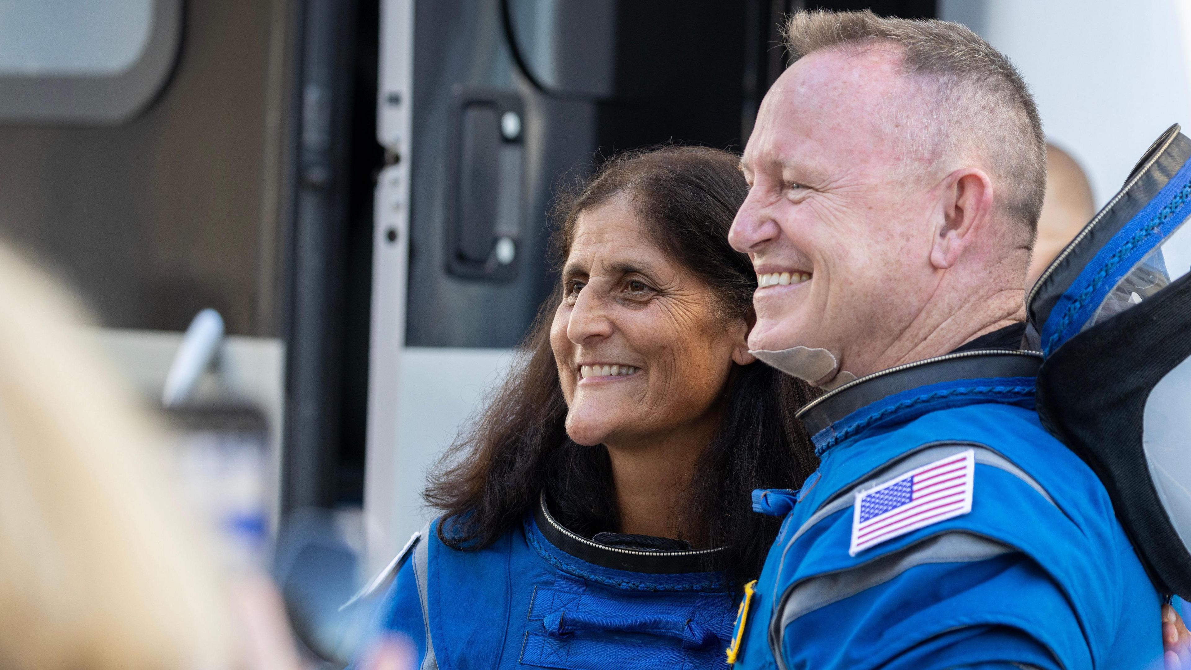 A female and male astronaut smile at a camera before a space launch