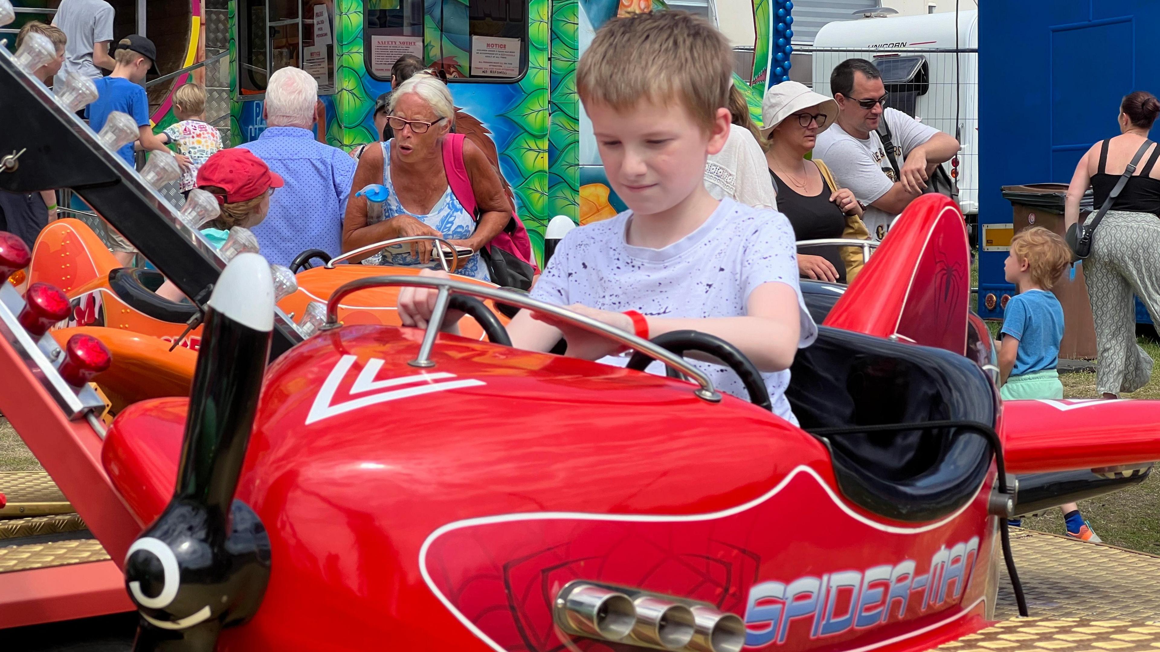 A boy sits in a plane attached to a ride as he plays with the steering wheel