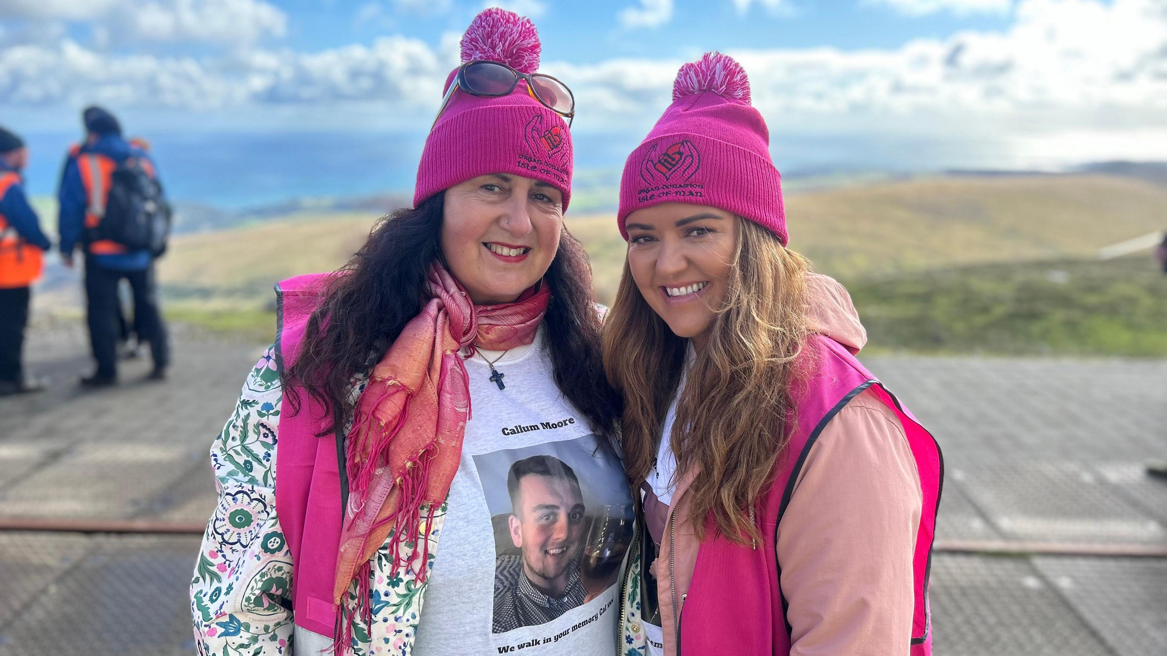 Sandra Moore and Rachael Cashin standing next to each other on Snaefell smiling and dressed in pink. Ms Moore is wearing T-shirt with a picture of her son, Callum Moore, printed on it.