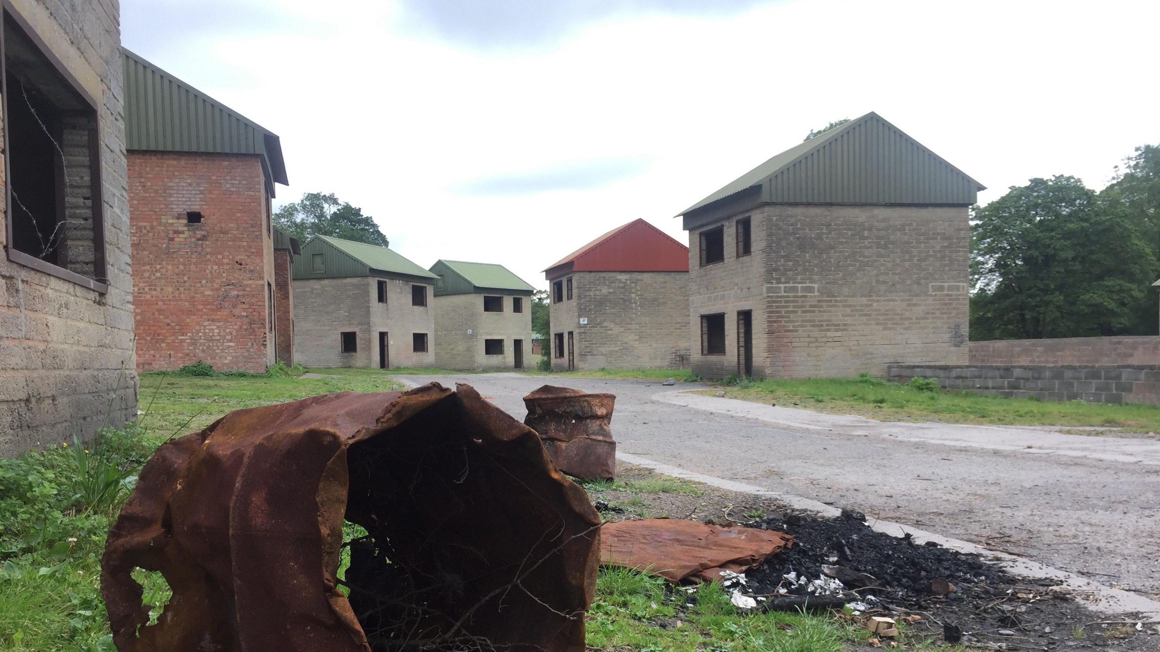 A burned out bit of metal barrel in the forefront of the picture. Behind are several house-like structures built for training