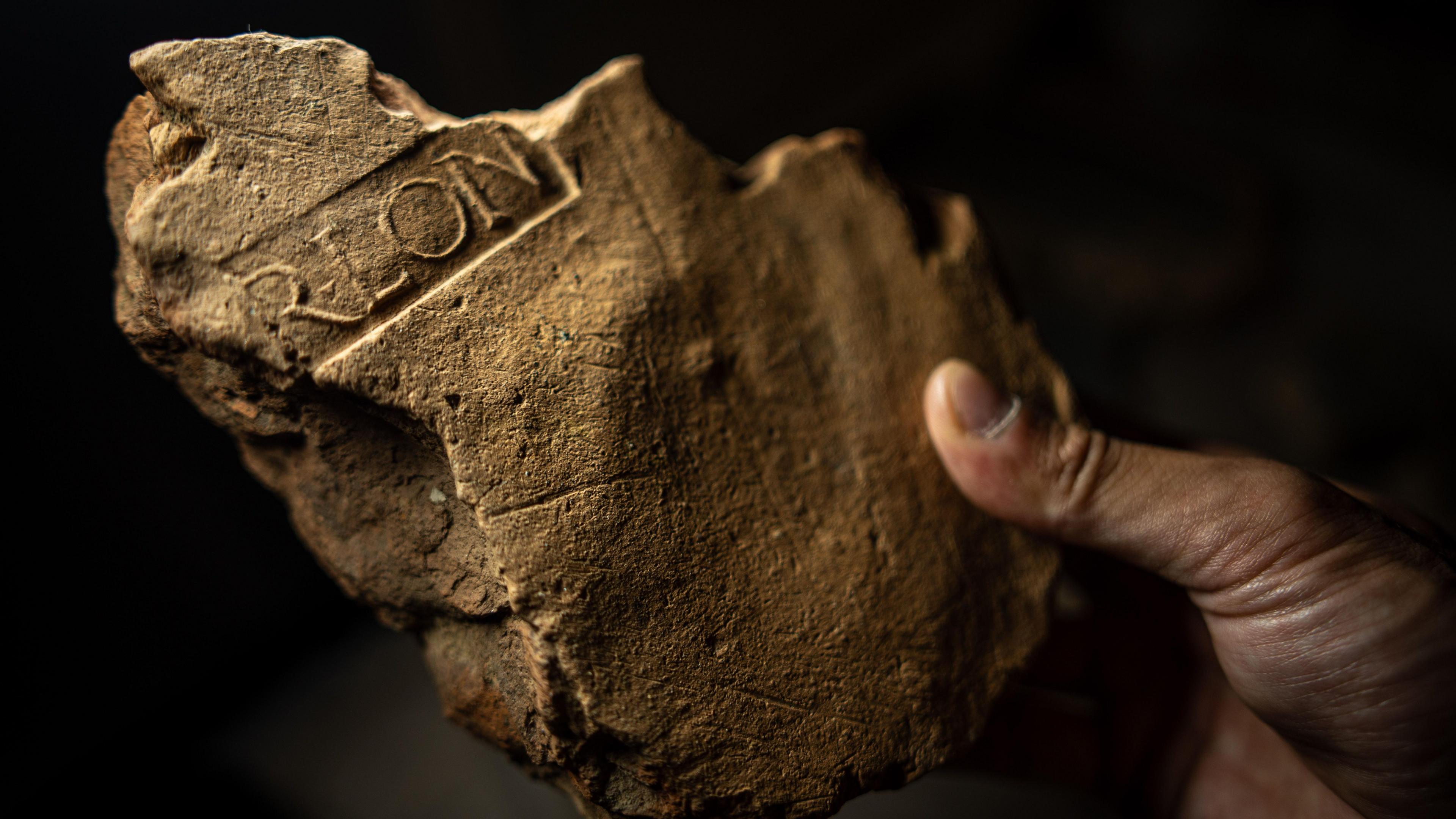 A close up of a broken piece of light brown stonework. Clearly visible are the remnants of some of the letters that have been imprinted in the plaster as it dried - R-L-O-N. It stands for Procurator of Londinium and shows that the building it was part of was a civil building in the growing city.