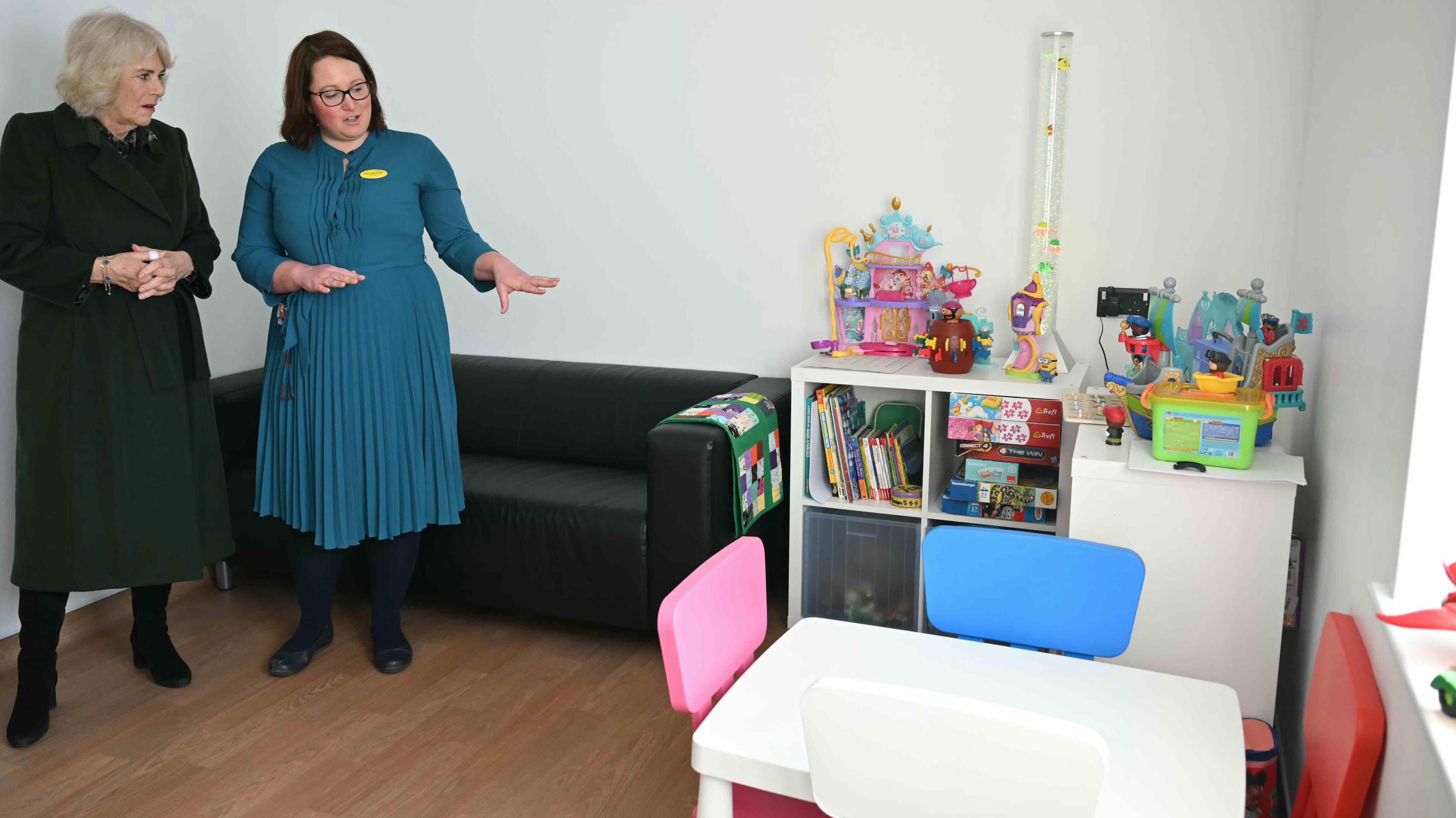 Queen Camilla (left) is shown a paediatric non-acute room with toys, a table and chairs and other furniture including a bookcase for children.