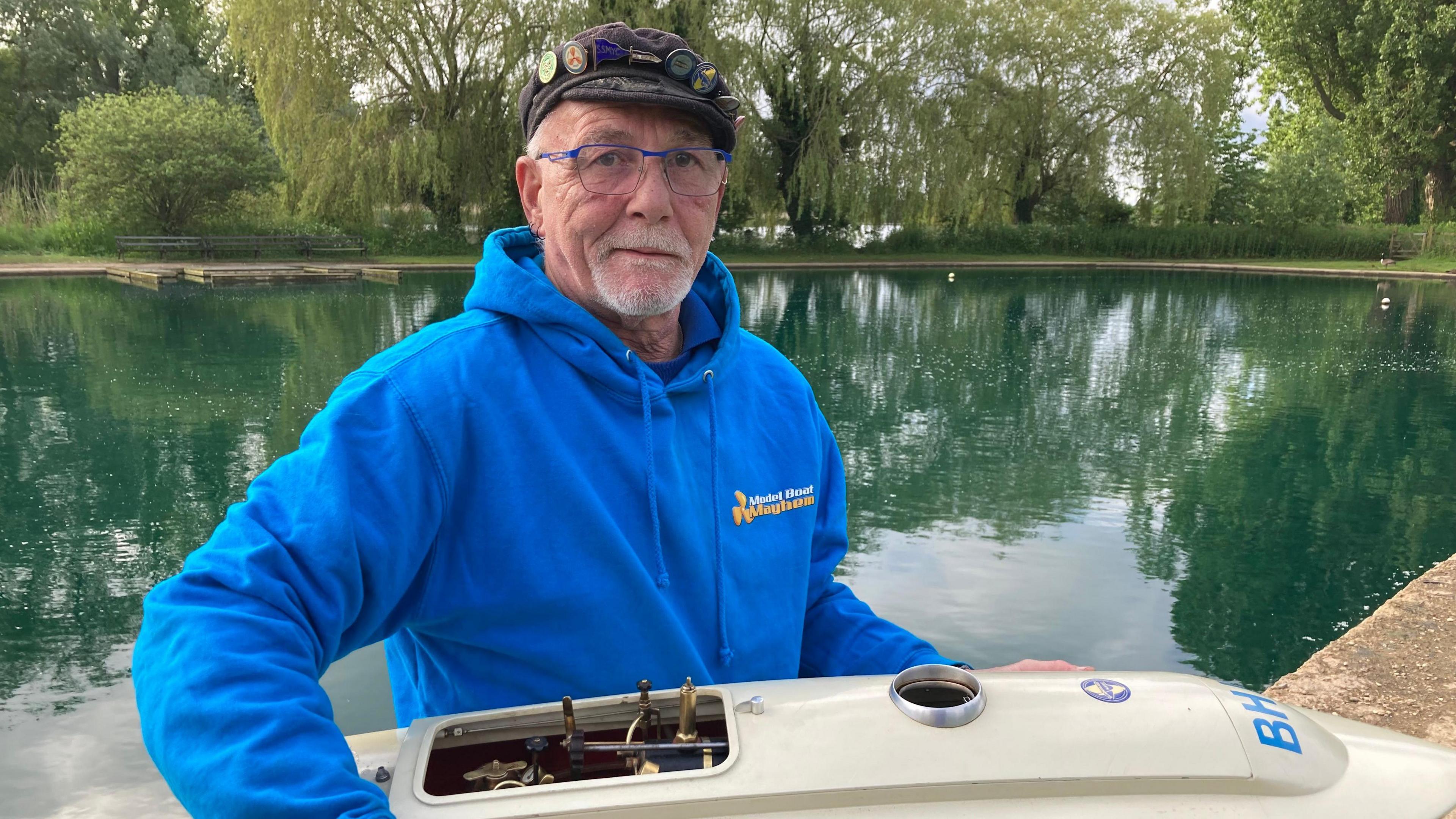 Man in a blue hoodie holding a white steam powered boat