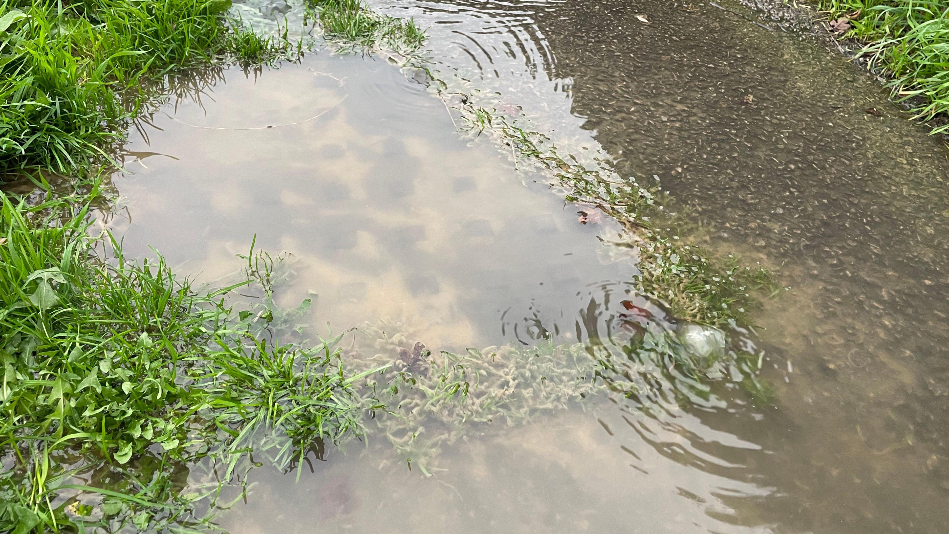 A pavement covered in water in the village of Hill Ridware in Staffordshire.  Brown solid matter and discoloration is visible in the water. 