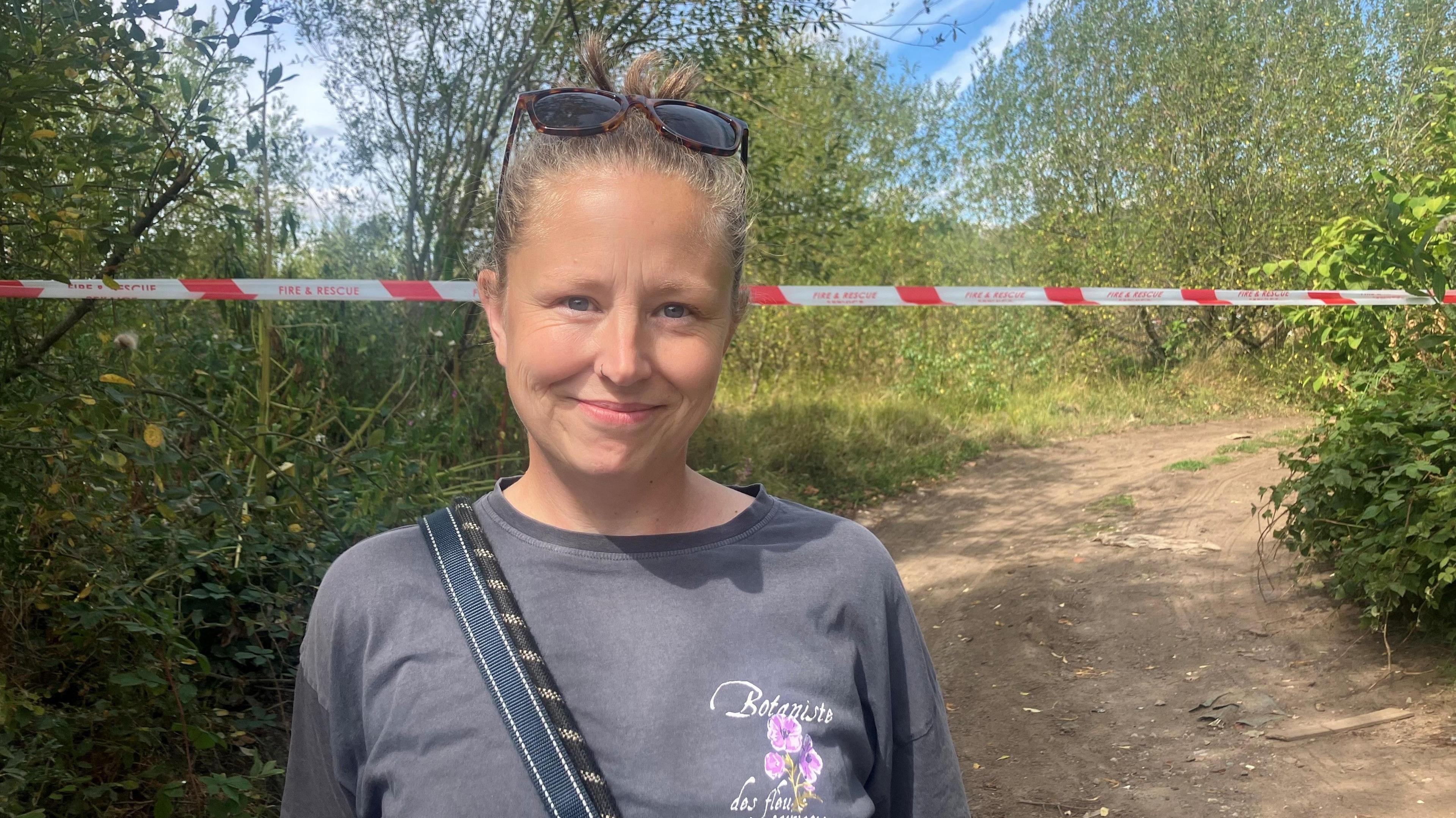 Photograph of dog-walker Laura Clinton. The image shows her in woodland, close to the scene of the fire, with exclusion tape in the background.