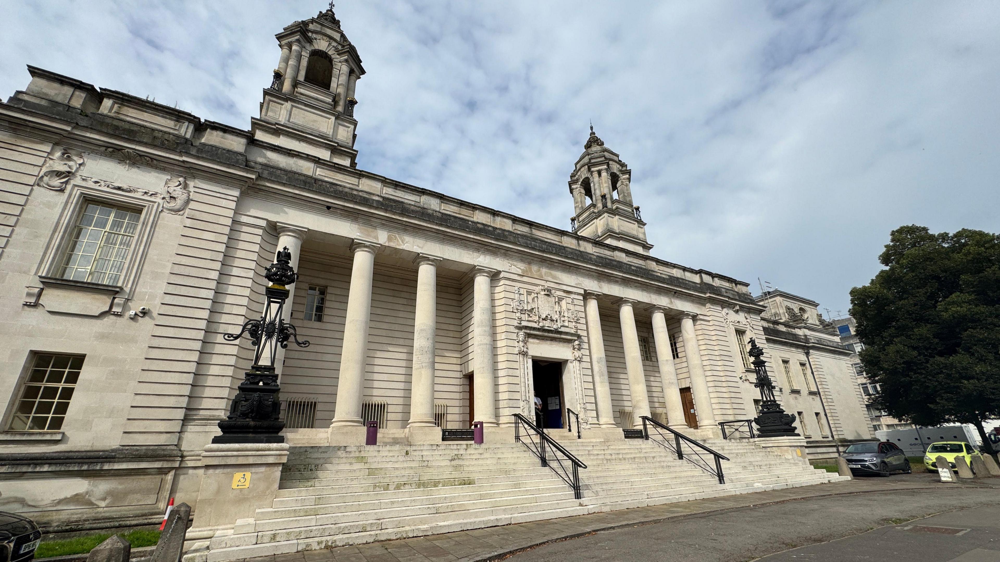 The outside view of Cardiff Crown Court. It is an Edwardian Baroque style building constructed with Portland stone. It has eight small columns and two turrets.