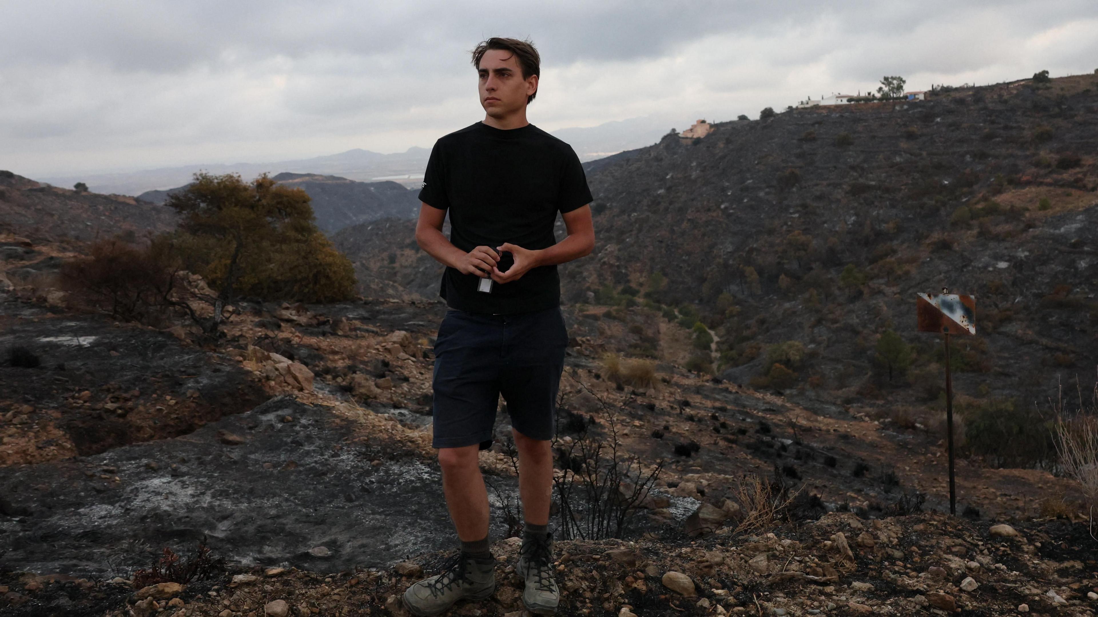 Dressed in a black t-shirt and back shorts, Thomas-Wolf Verdonckt stands on the charred landscape in Bedar, Spain, where his father was killed during the deadly wildfires.
