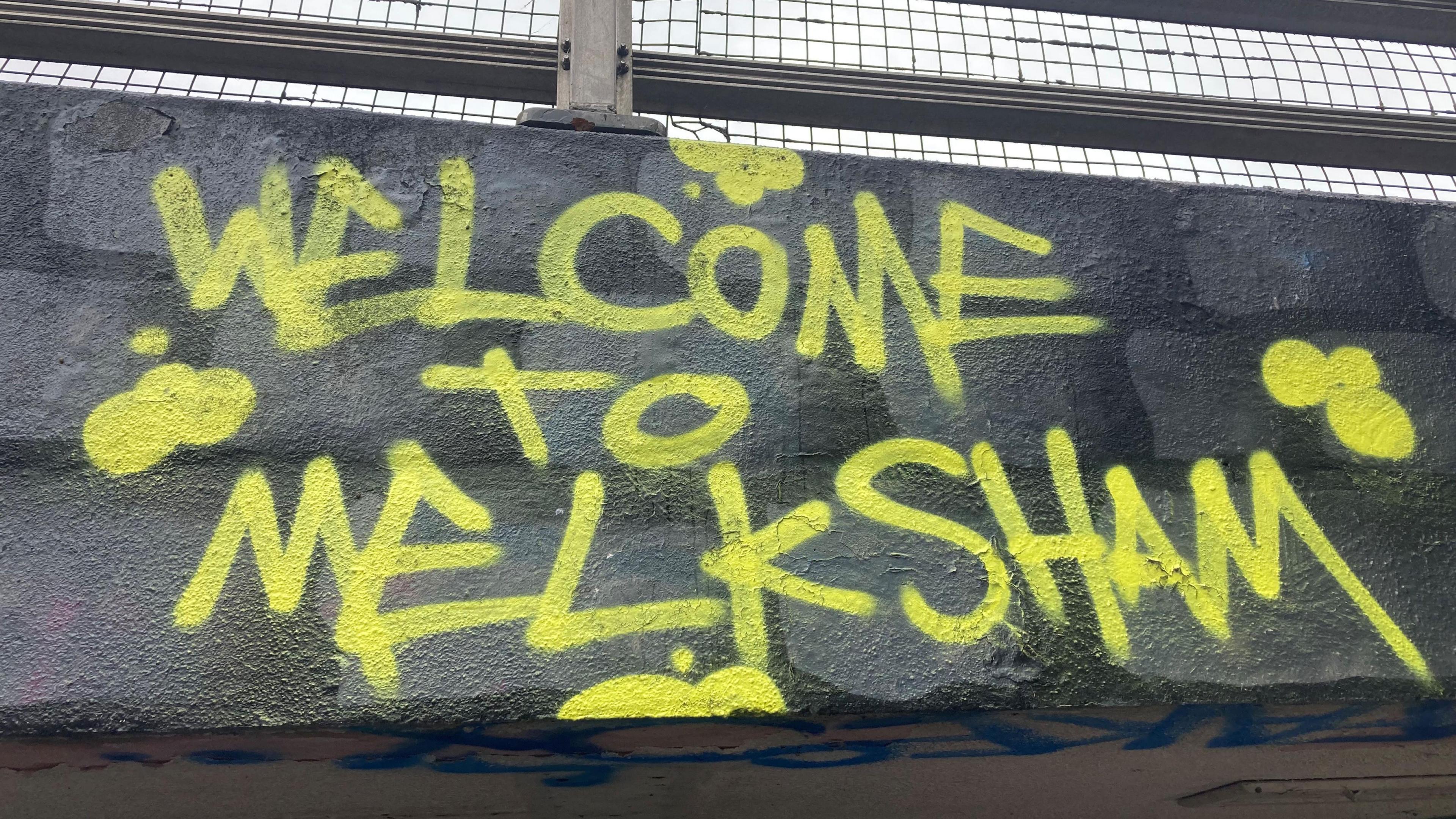 A wall with yellow graffiti on it reading "Welcome to Melksham".