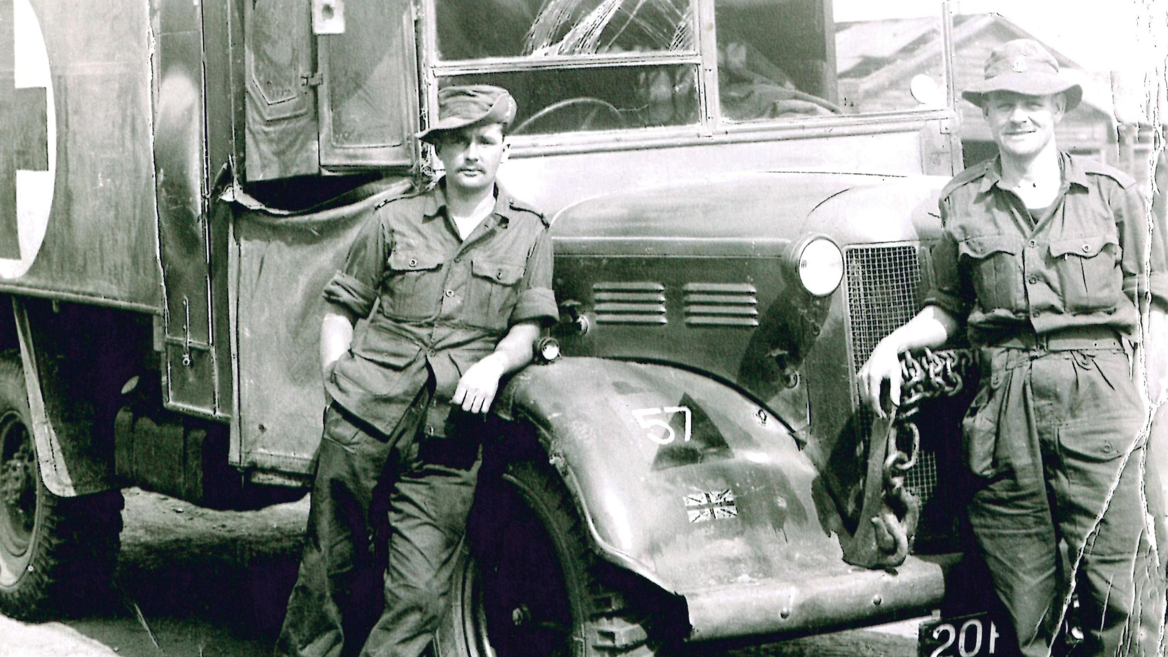 Two men standing beside ambulance vehicle, wearing military uniforms