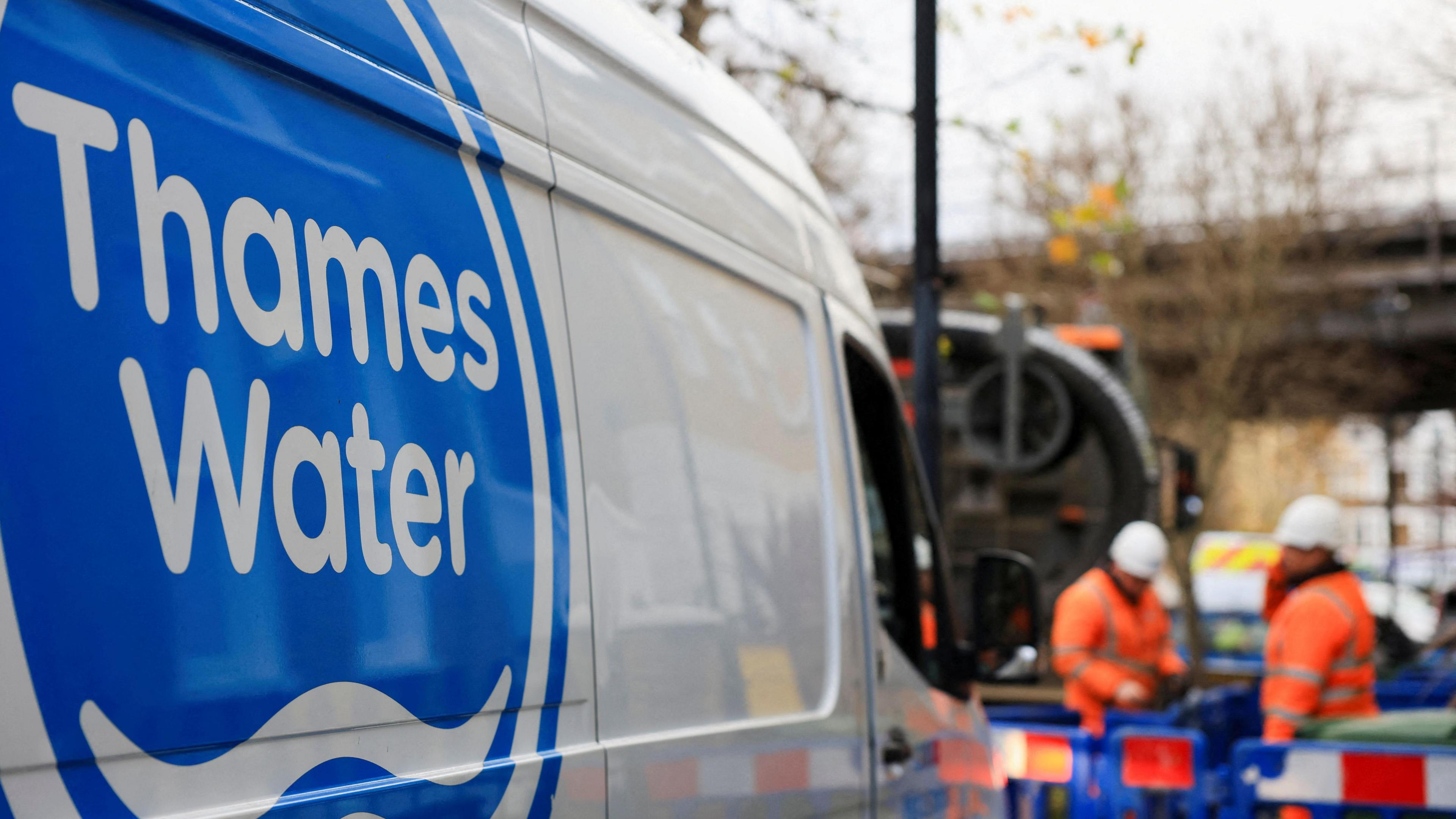 Thames Water employees carry out repair and maintenance in London. A van with Thames Water written down the side can be seen with two workmen in orange outfits further down the road.