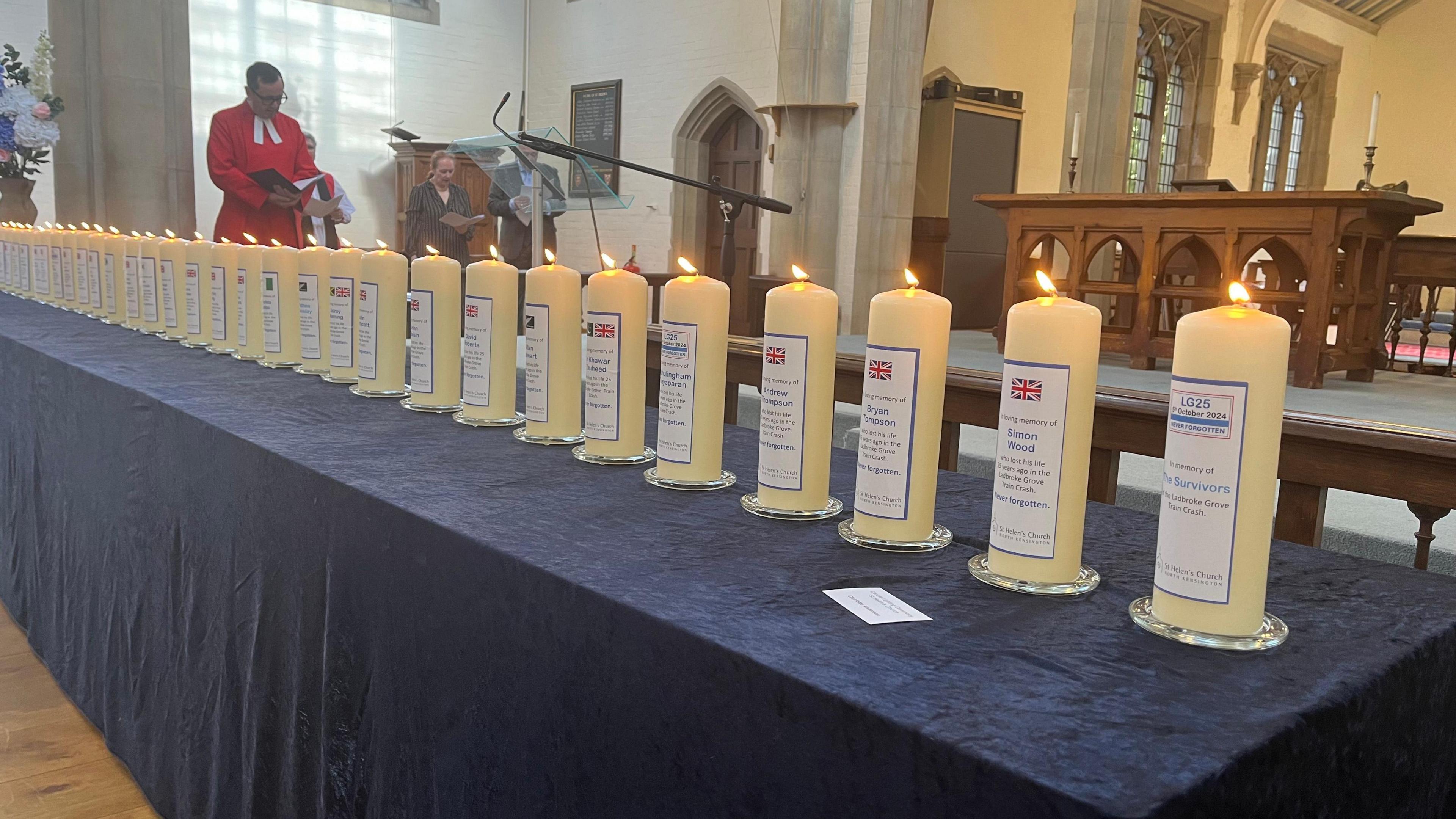 Large white candles on a table covered with a blue table cloth which were lit to mark 25 years since the Ladbroke Grove rail disaster