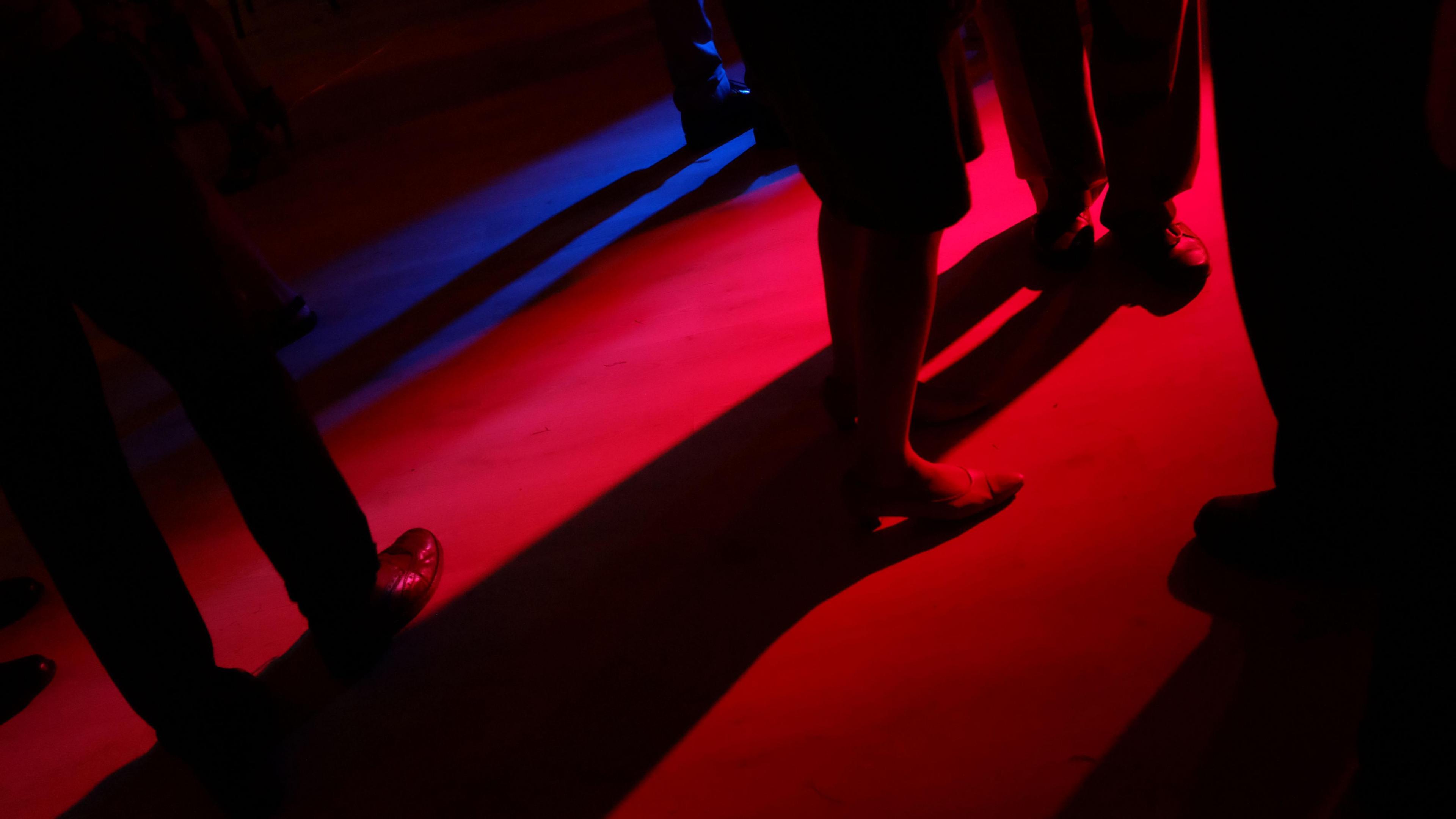 People's legs on a darkly-lit dance floor.