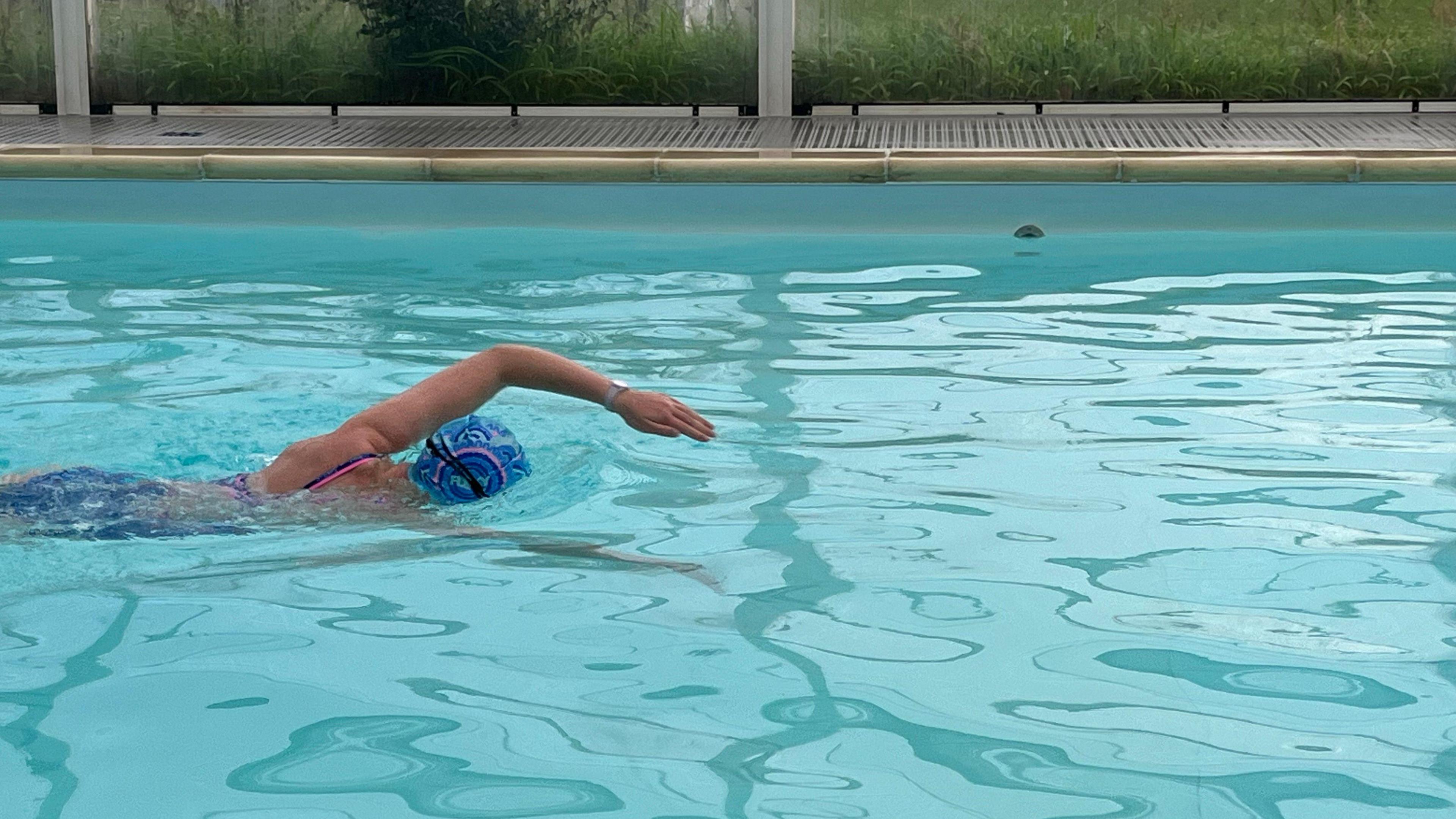 Chloe swimming in her local pool. She is wearing a blue swimming cap and goggles and is doing front crawl.