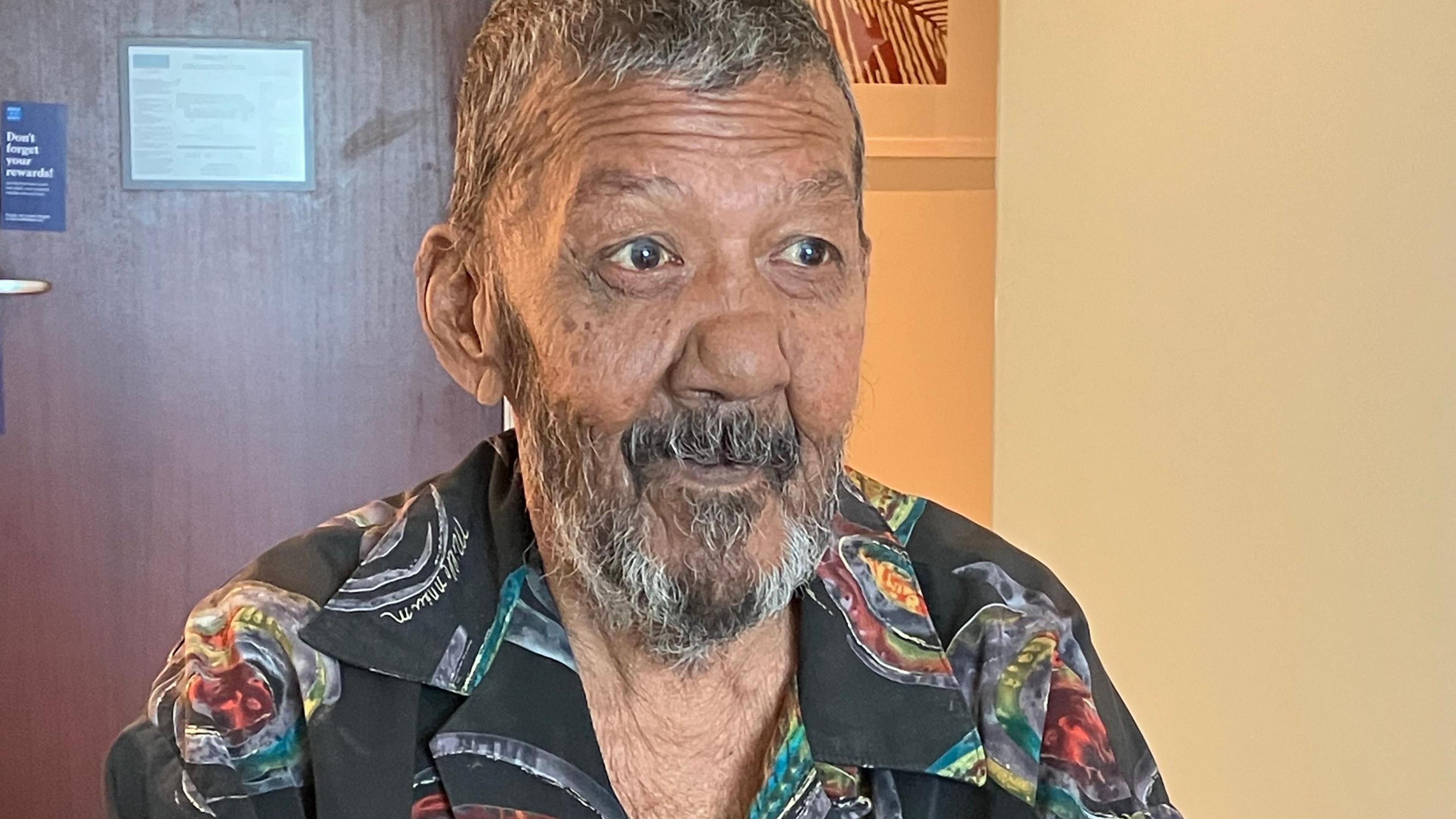 A man with a beard, wearing a black and coloured shirt