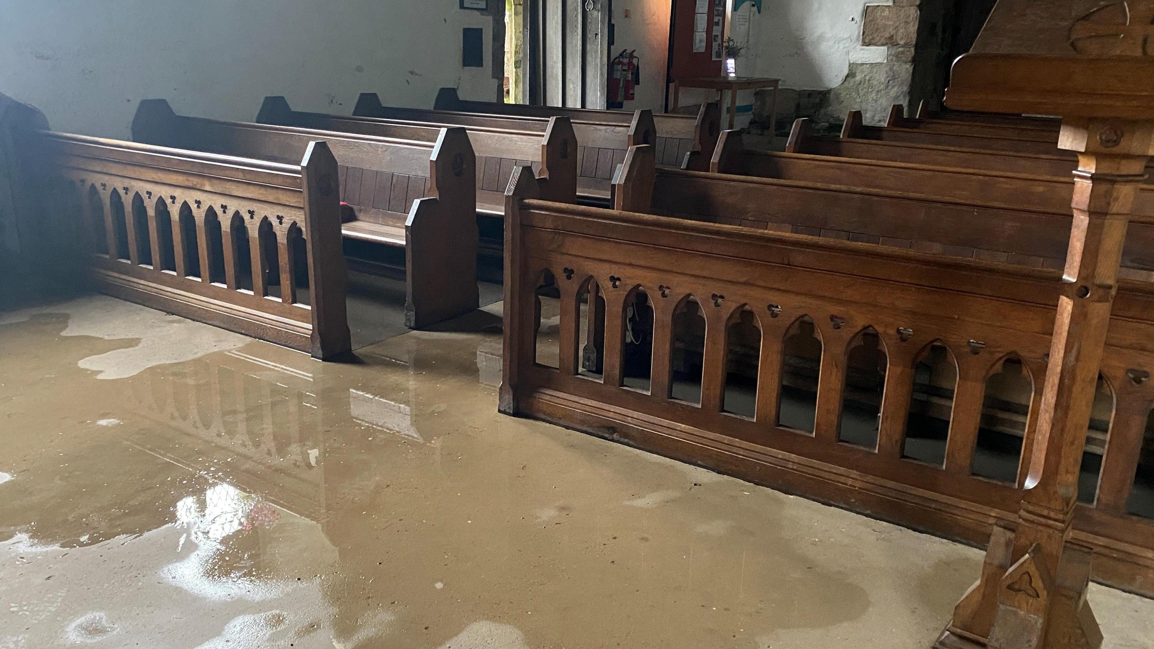 The inside of a church with wooden pews and water on the floor 