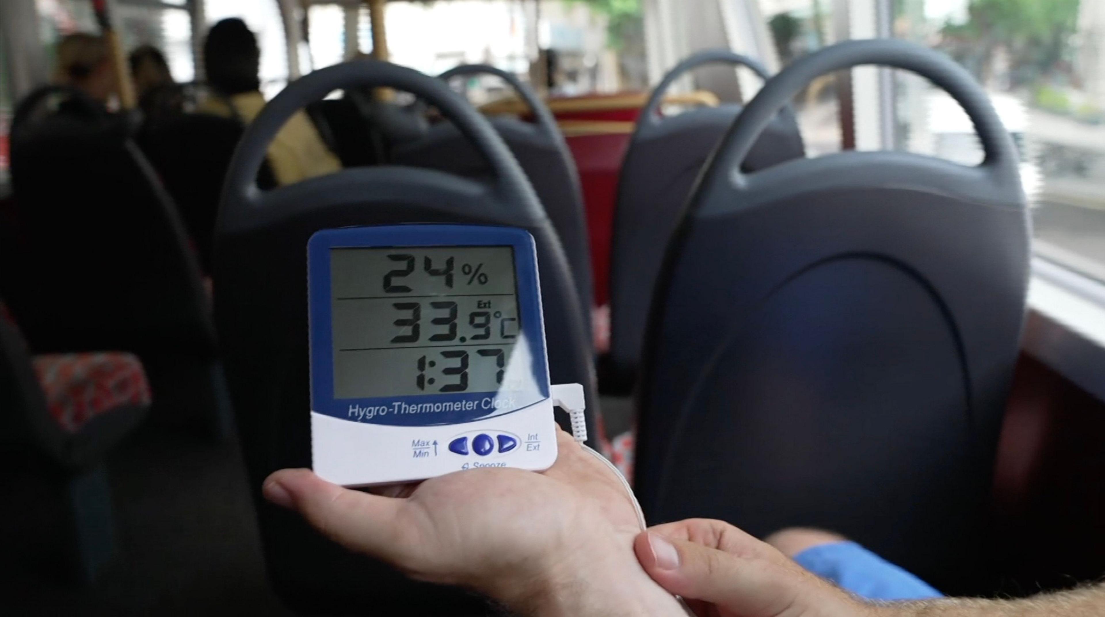 A thermometer on a bus shows 33.9C with 24% humidity at 1.37pm. In the background are the backs of bus chairs and passengers
