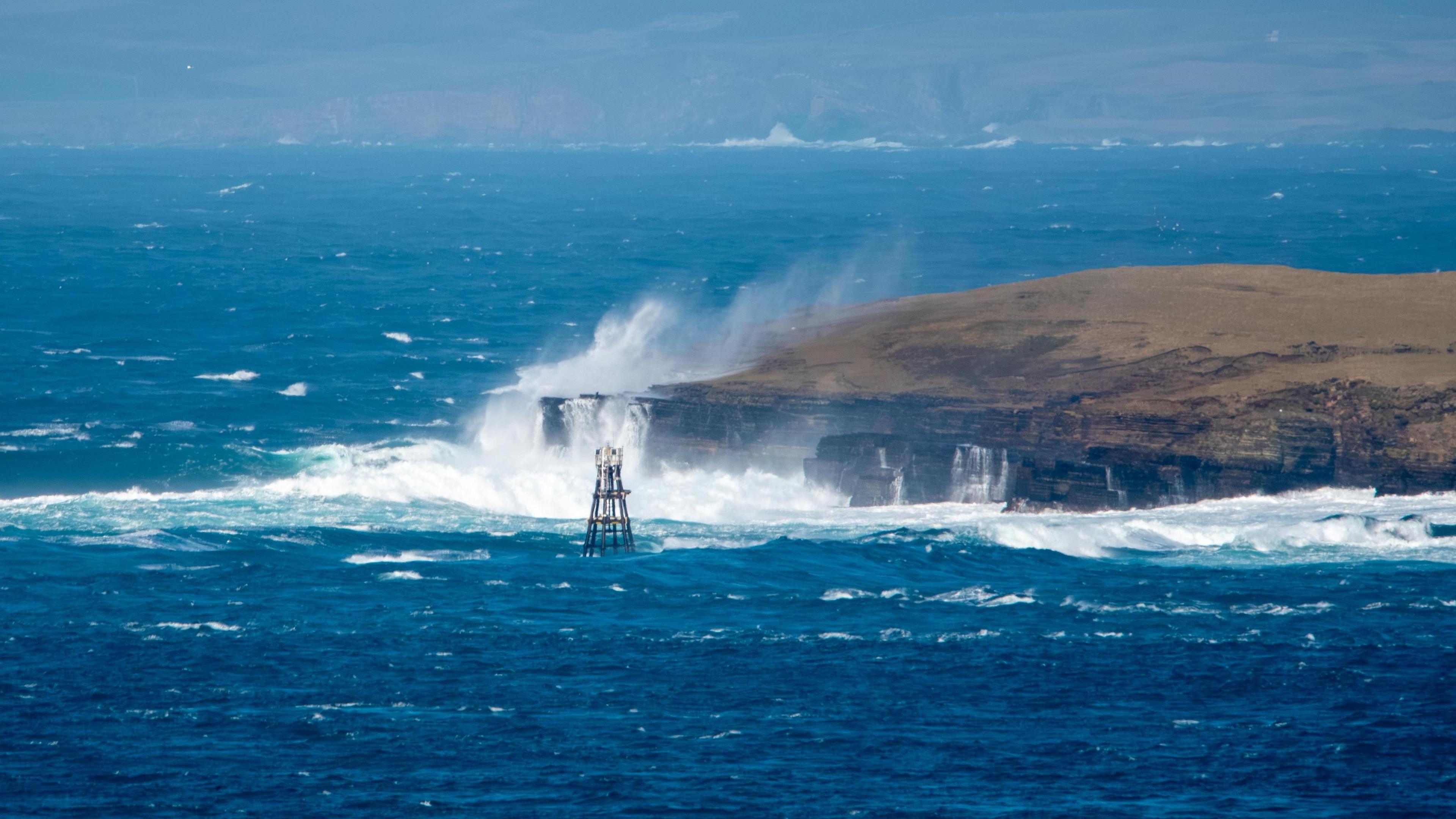A rough sea where large waves are crashing into a headland sending splashes of water high into the air