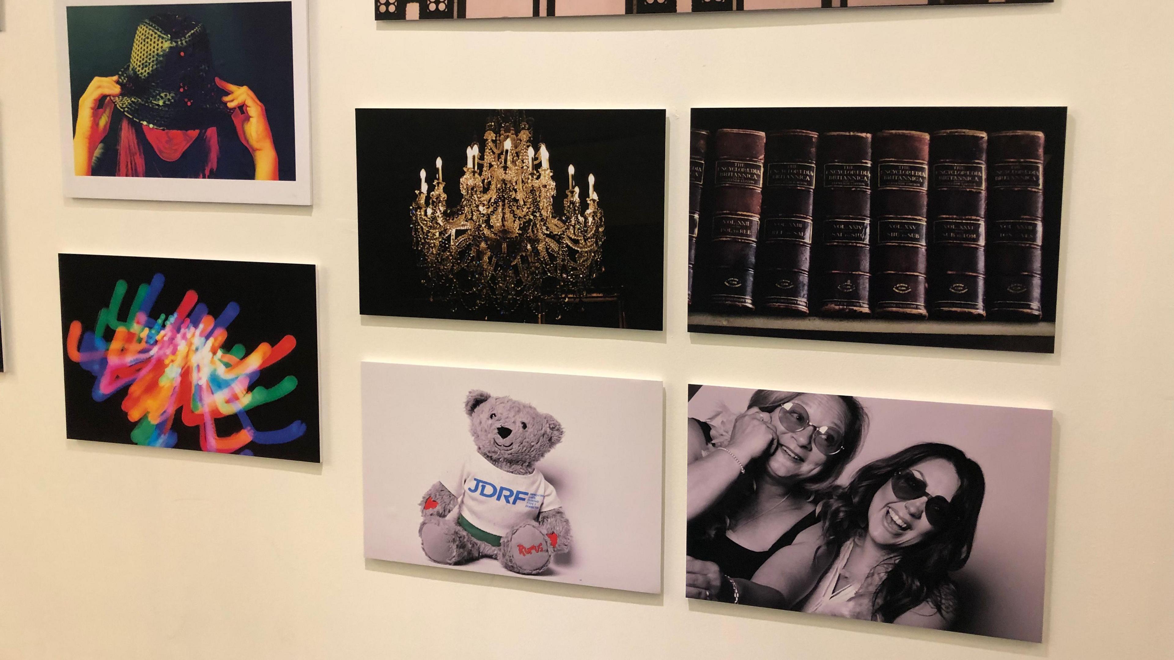 Several photographs on a display wall, including a teddy, a chandelier, and some old books