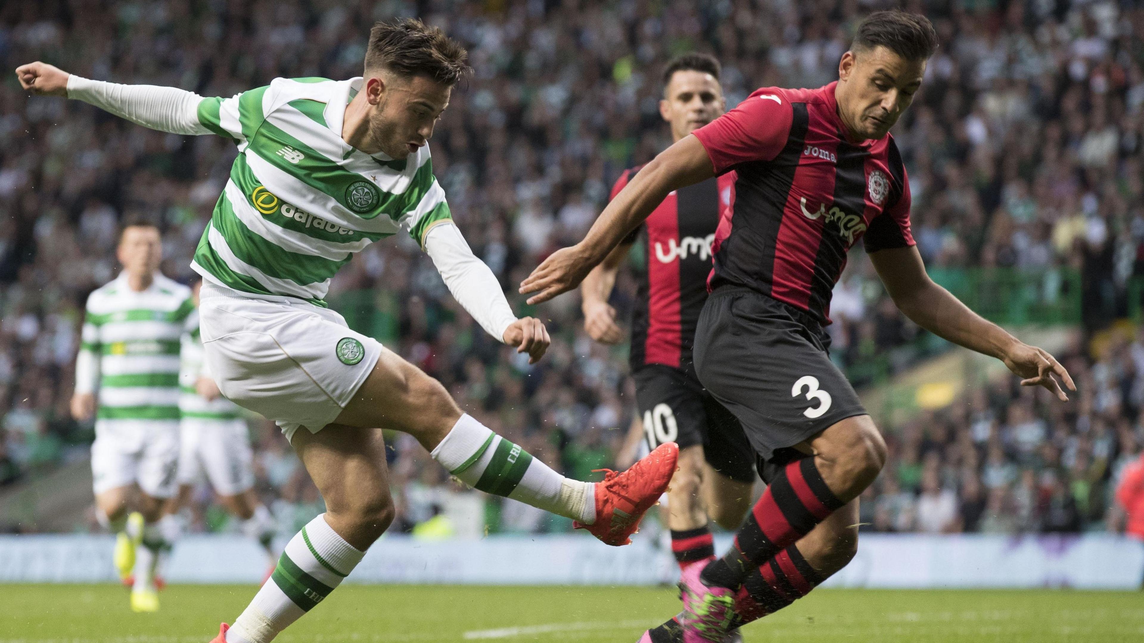 Patrick Roberts, wearing Celtic's green and white hoops, shoots for goal while being covered by a Red Imps defender, wearing red and black stripes.