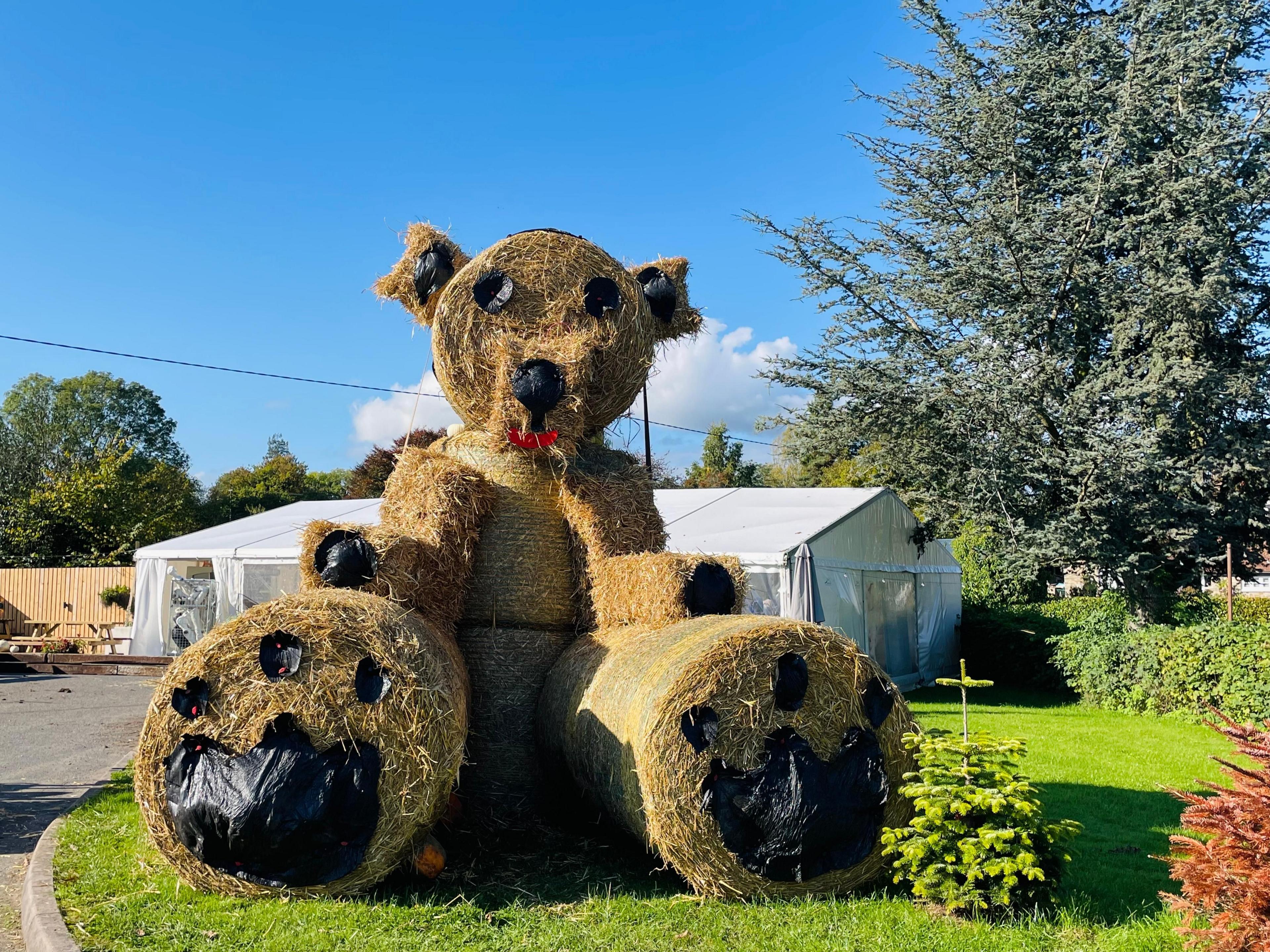 A large teddy bear sculpture made of round straw bales with plastic facial details and paws added.