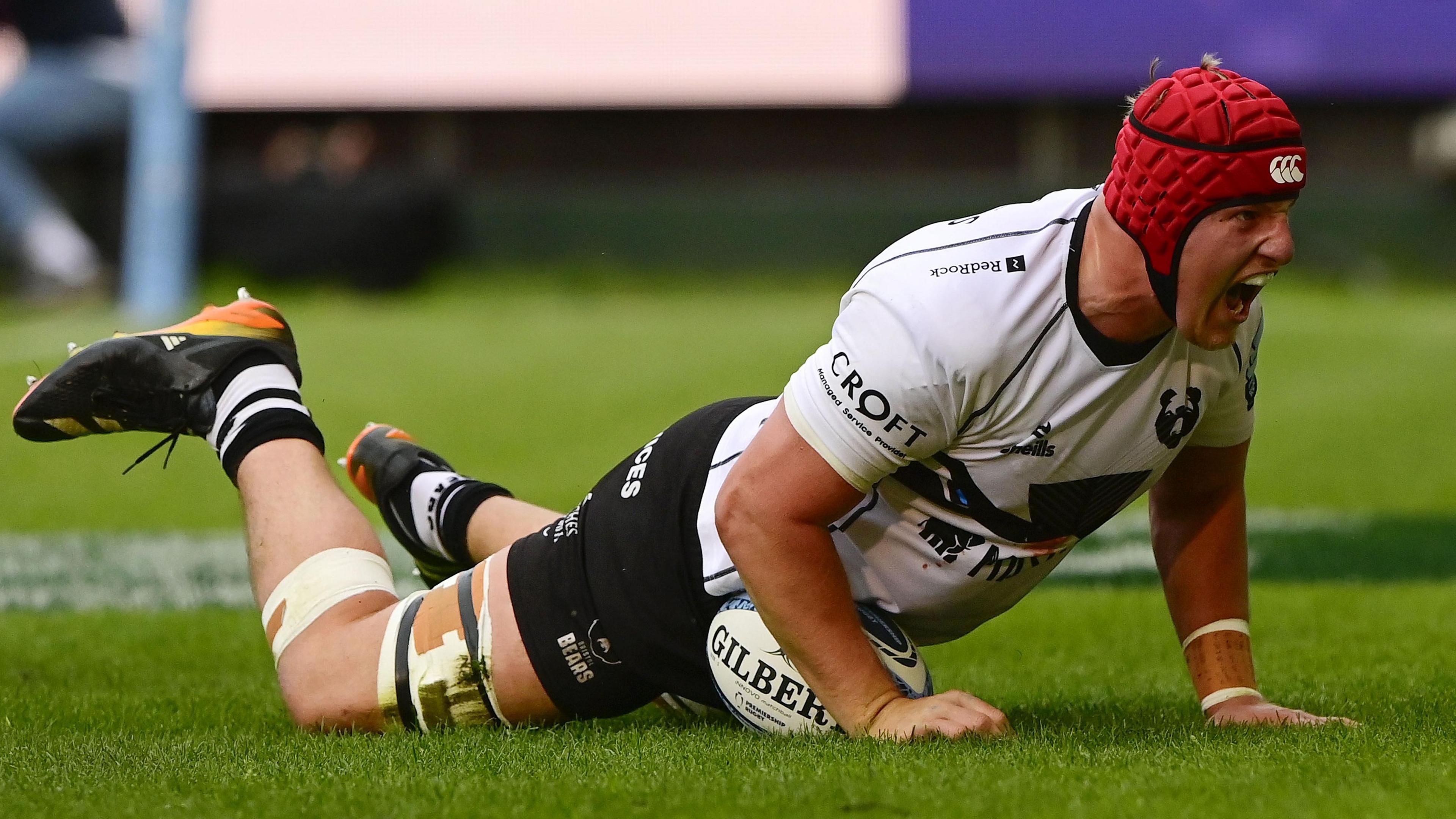 James Dun celebrates while lying down on top of a rugby ball after scoring a try for Bristol Bears