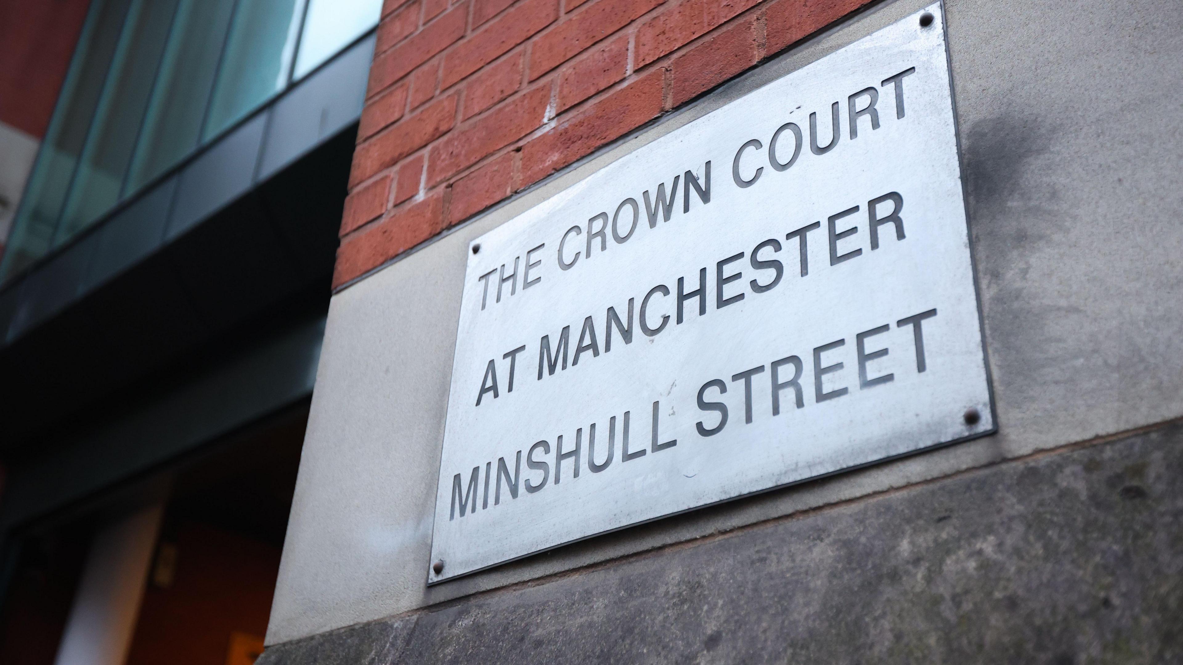 A close-up of a metal sign bolted to a brick wall which states 'The Crown Court at Manchester Minshull Street'. 