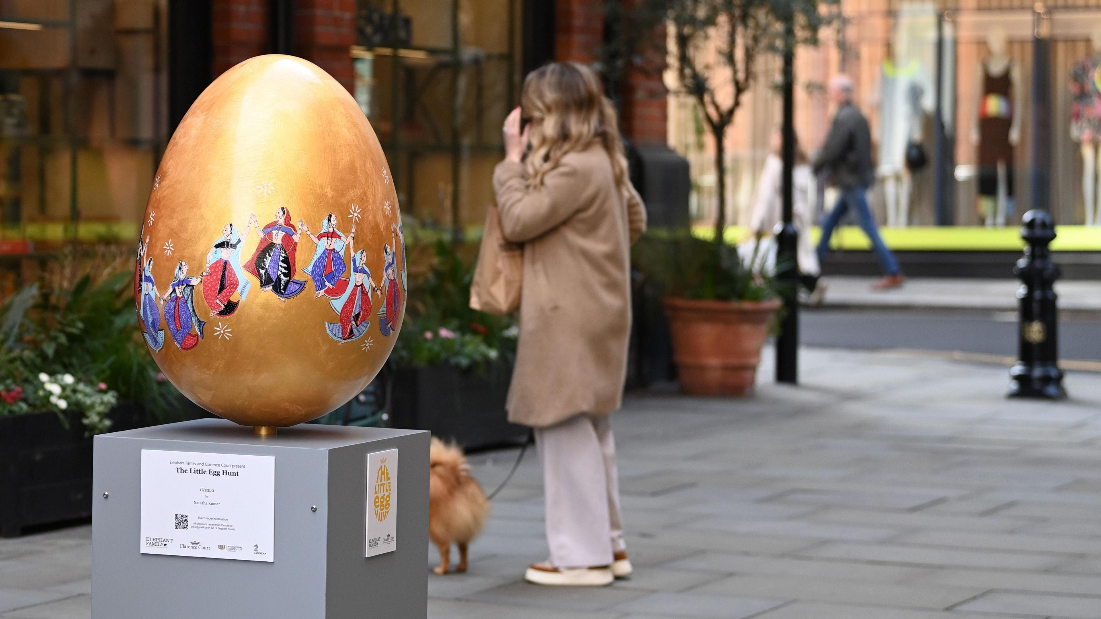 A golden egg with ladies drawn around it wearing blue, red and purple and holding hands.