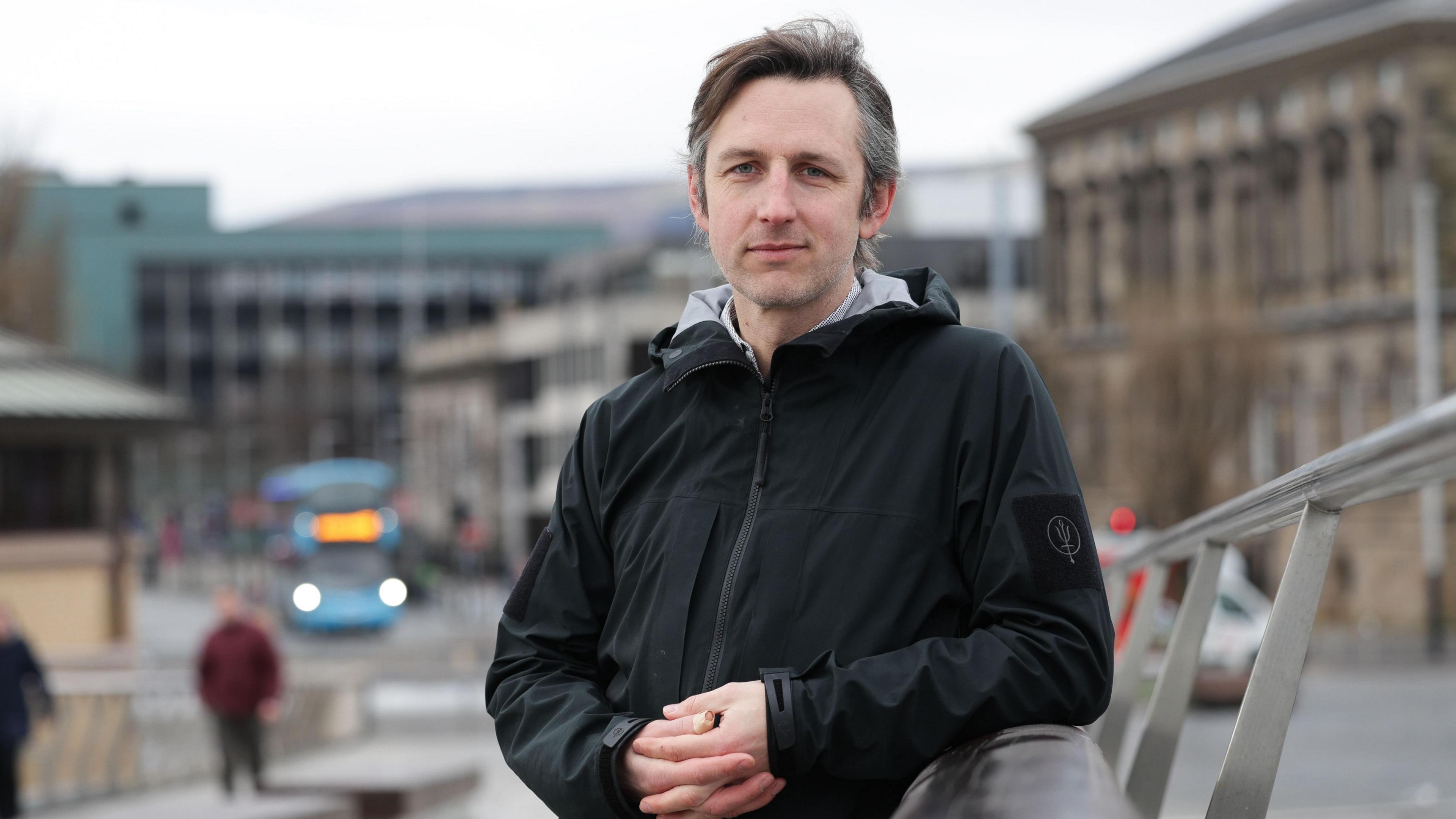 Earl of Shaftesbury wearing black rain jacket leans over a railing in Belfast city centre