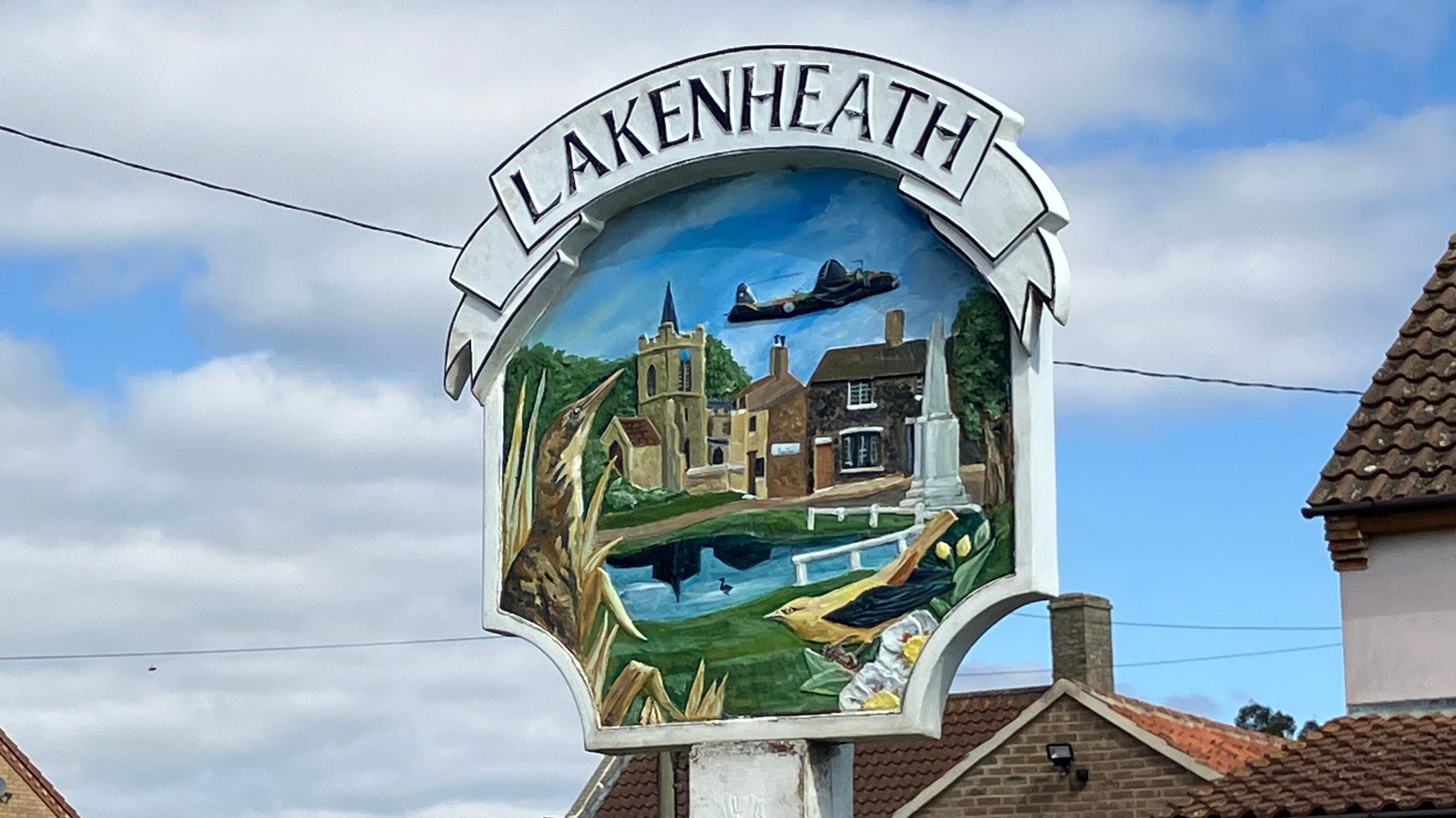 The Lakenheath village sign. The village name is written above a depiction of the village which includes a plane for the nearby RAF base.