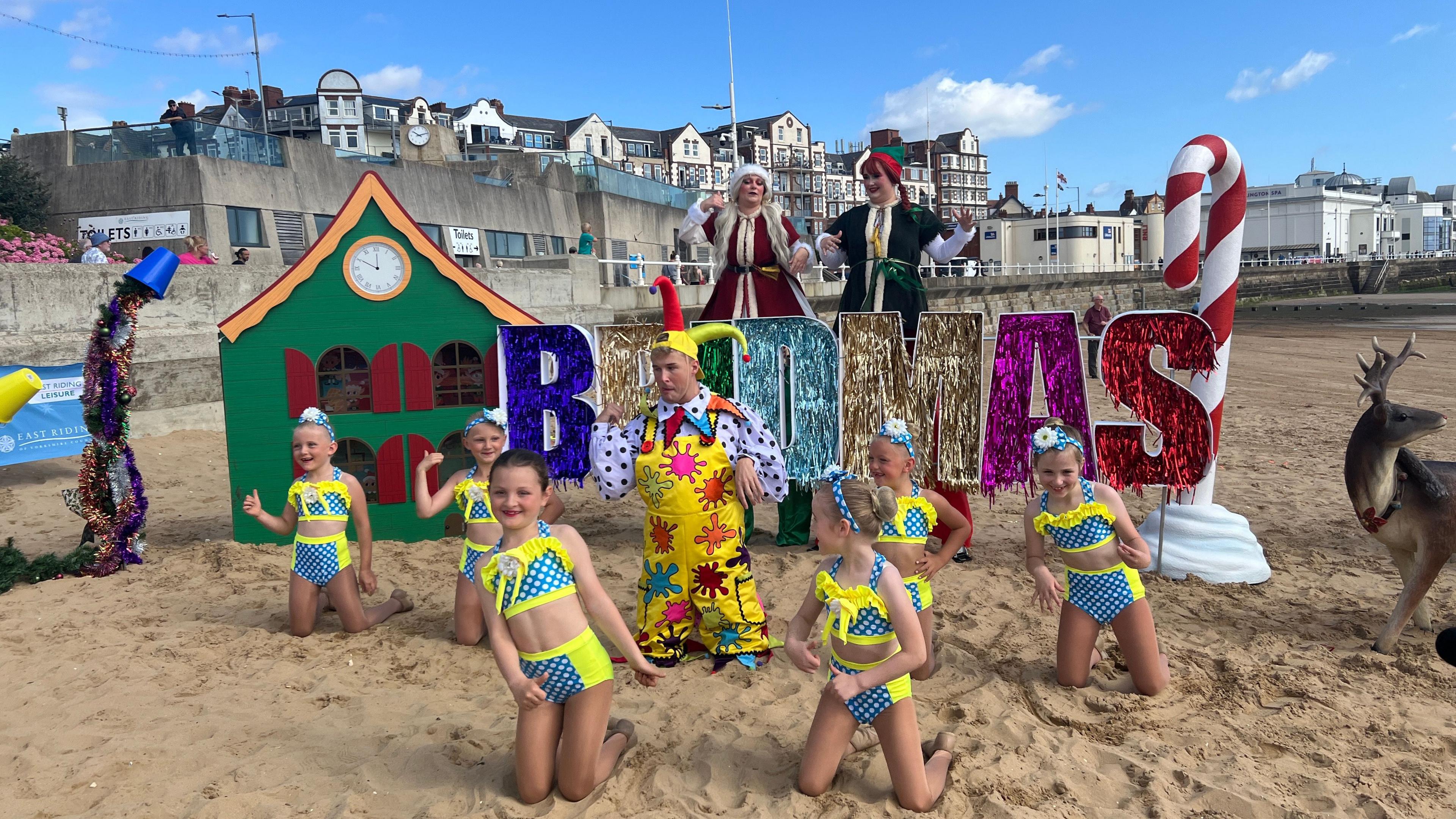 A group of young girls dance on the beach with the Bridlinton panto star and the stilt walkers