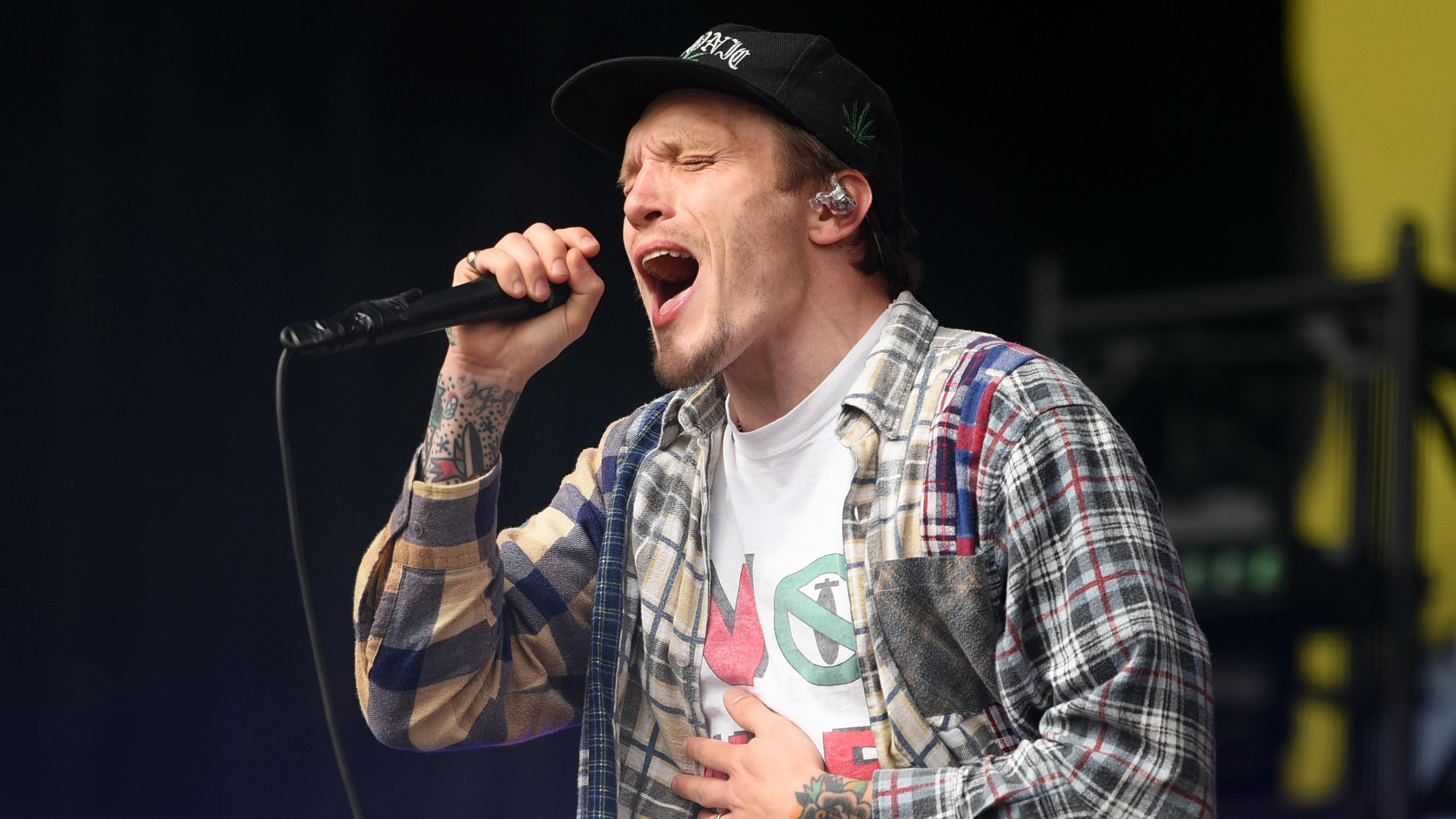 Ben Barlow, wearing a check shirt, of Neck Deep belts into a microphone on the main stage at Leeds Festival