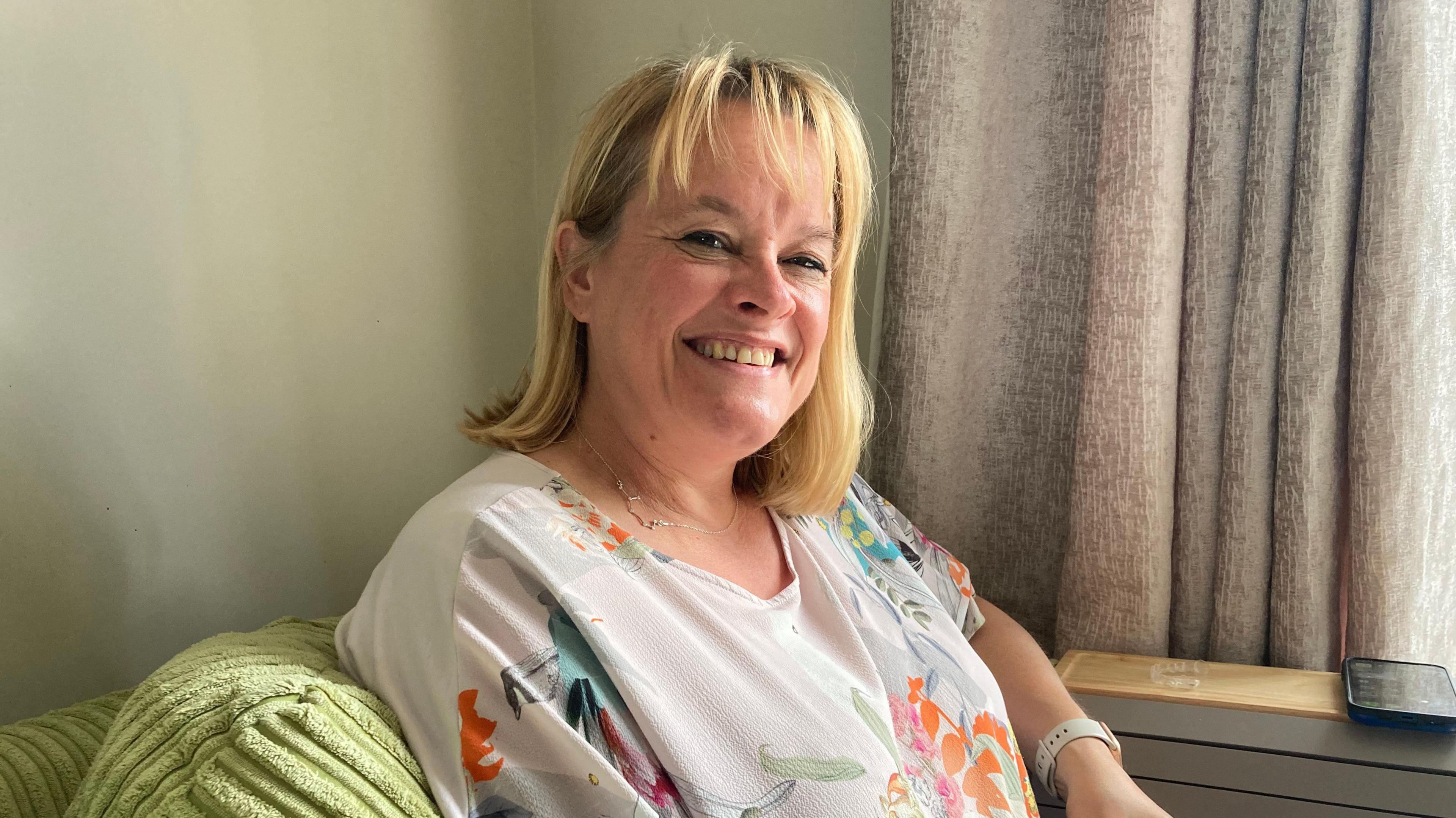 A woman wearing a blouse with a floral pattern while sat on a sofa